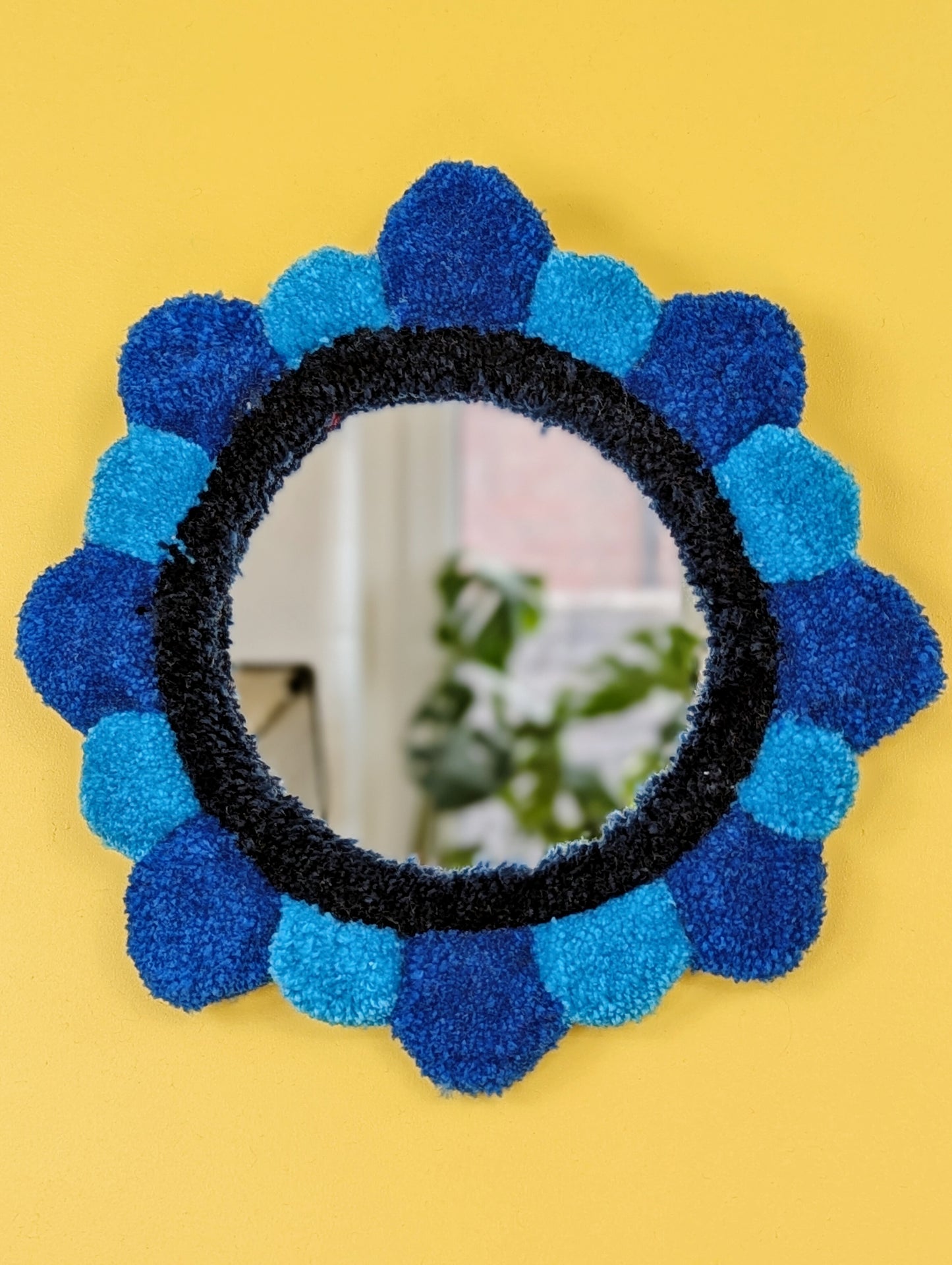 Handmade tufted petal mirror with blue textured yarn petals surrounding a round mirror