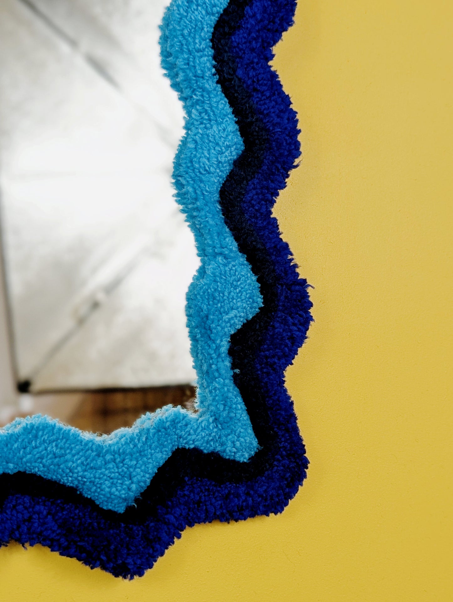 Handmade wavy tufted mirror with colourful textured frame in alternating shades of blue, modern aesthetic wall décor for home interiors.