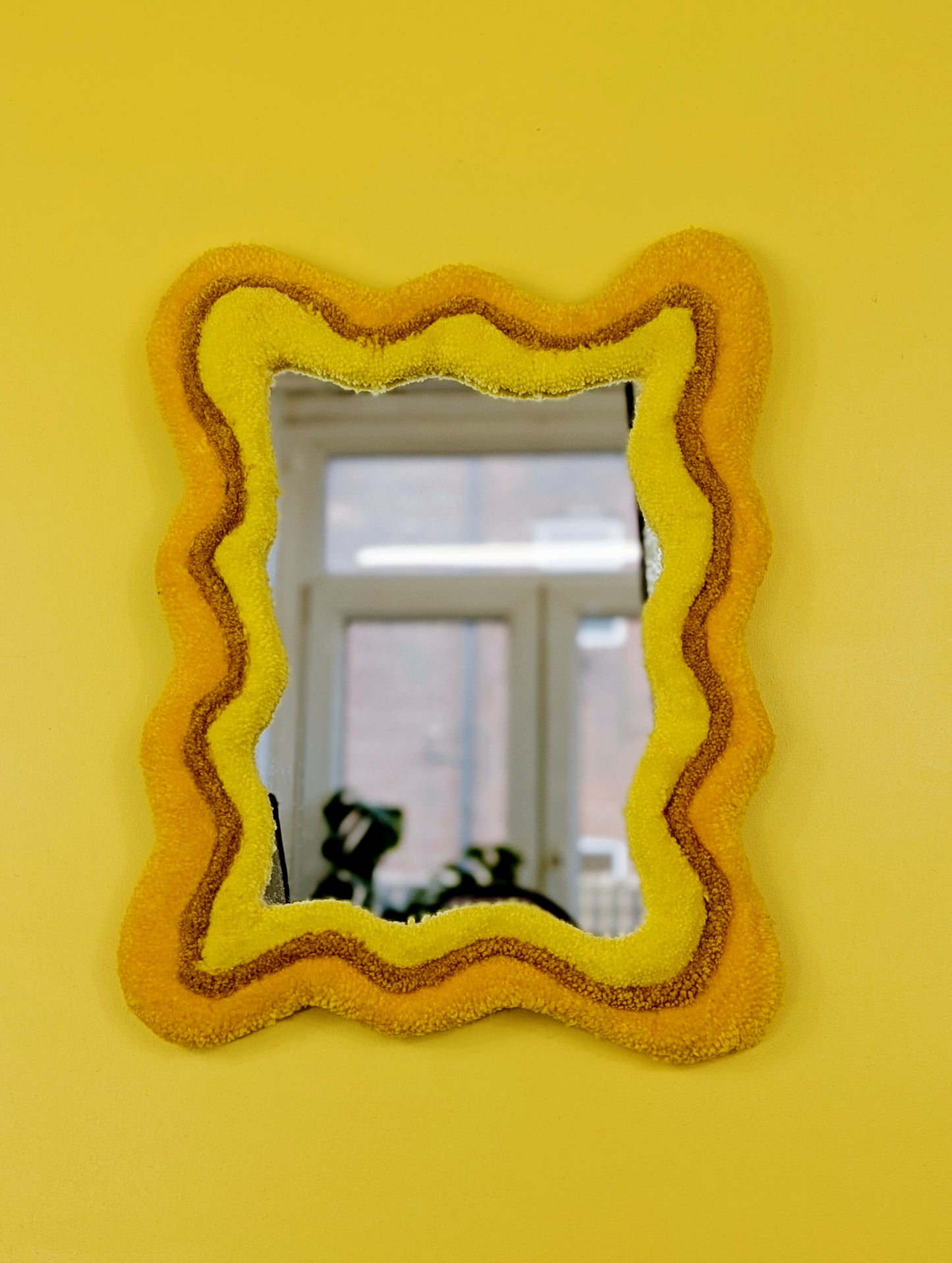 Handmade wavy tufted mirror with colourful textured frame in alternating shades of sunshine yellow, mustard yellow and bright yellow, modern aesthetic wall décor for home interiors.
