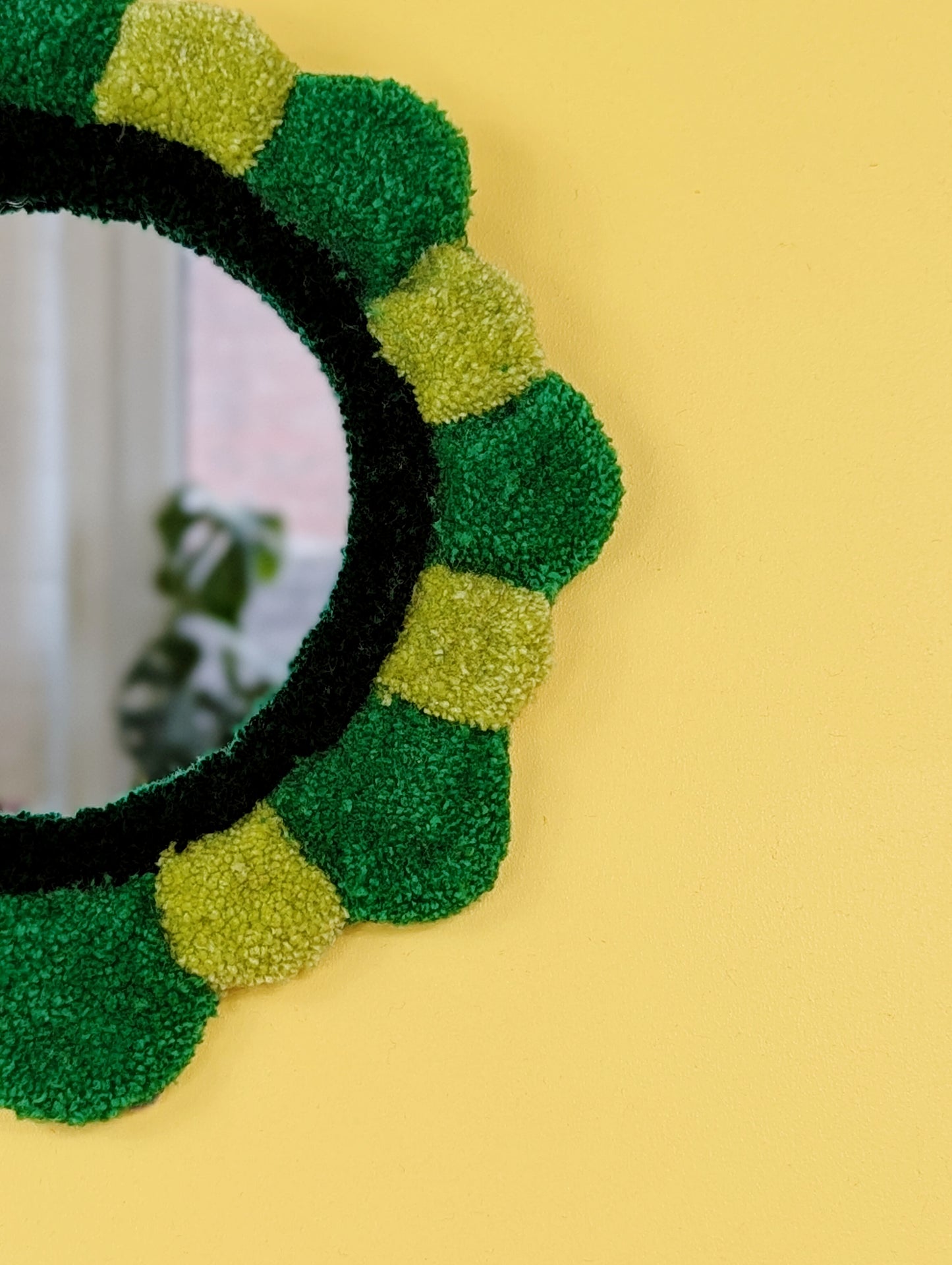 Handmade tufted petal mirror with green textured yarn petals surrounding a round mirror