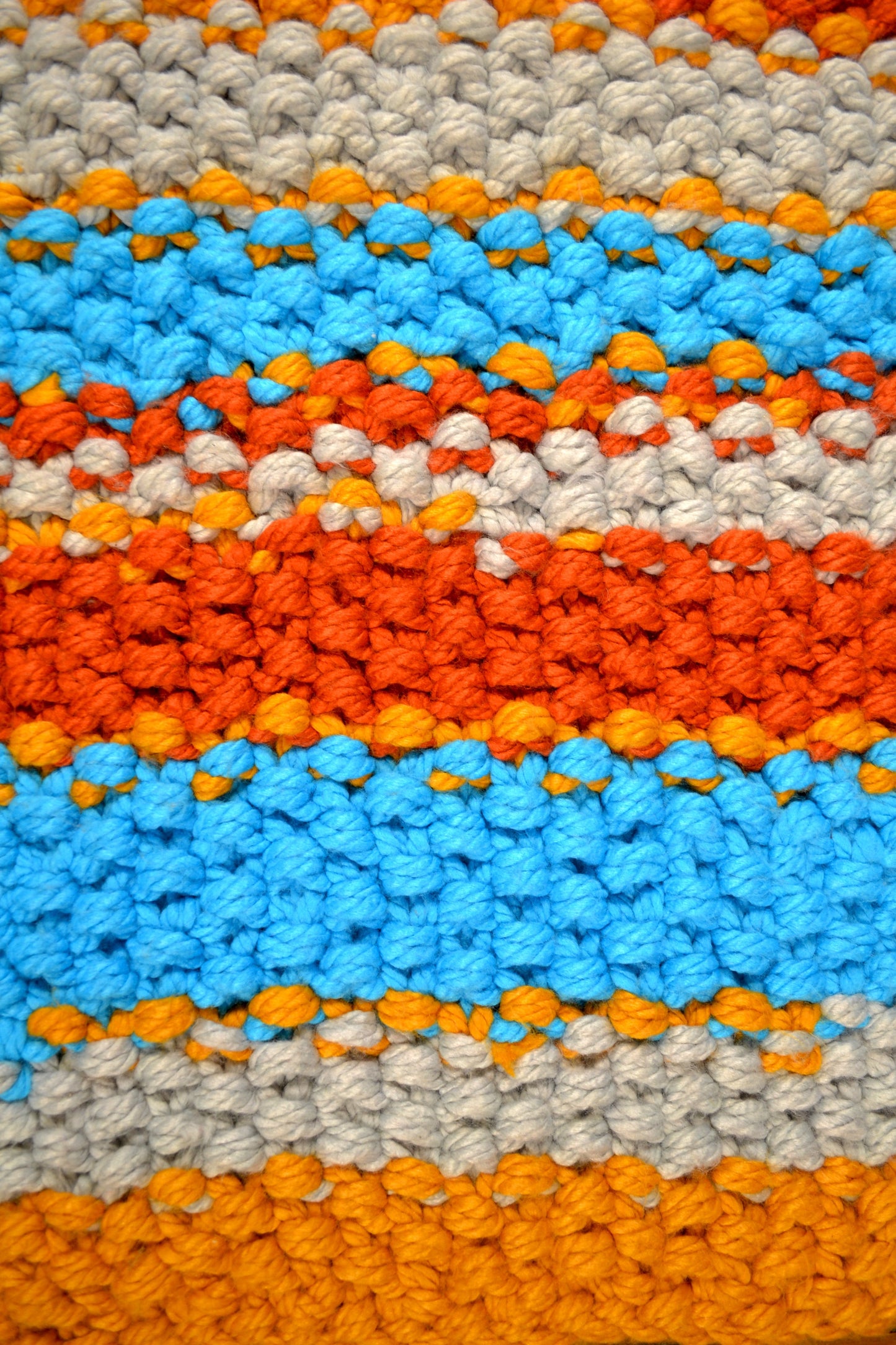 Zoomed in image of striped rug, showing detailing of individual stitches. Rug has a striped pattern. Rug is mustard yellow, burnt orange, grey and crisp sky blue stripes, with thick mustard yellow stripes at both ends. Each individual stitch is visibly and the rug has an extra thick pile height.