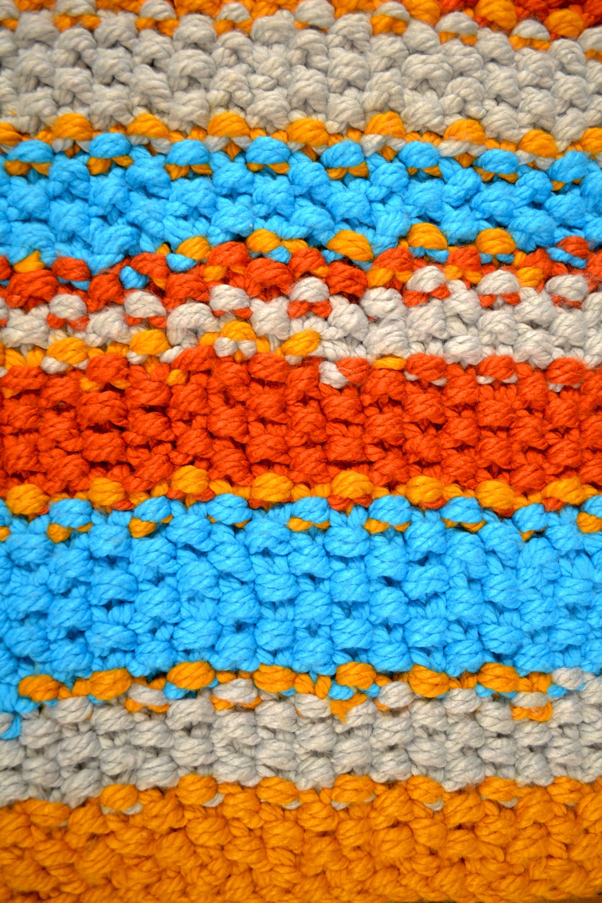 Zoomed in image of striped rug, showing detailing of individual stitches. Rug has a striped pattern. Rug is mustard yellow, burnt orange, grey and crisp sky blue stripes, with thick mustard yellow stripes at both ends. Each individual stitch is visibly and the rug has an extra thick pile height.