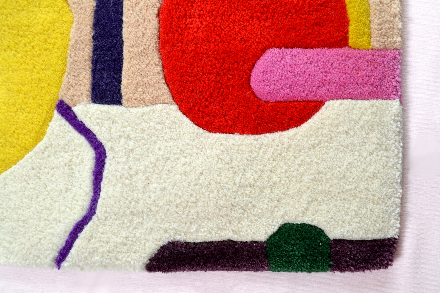 Image shown is off a corner of the cream rug. This section of the rug has a big red circle with hot pink band across it, a dark green semi-circle located at the bottom edge of the rug and a purple vein feature running down the cream background. The rug is photographed against a very pale pink background.