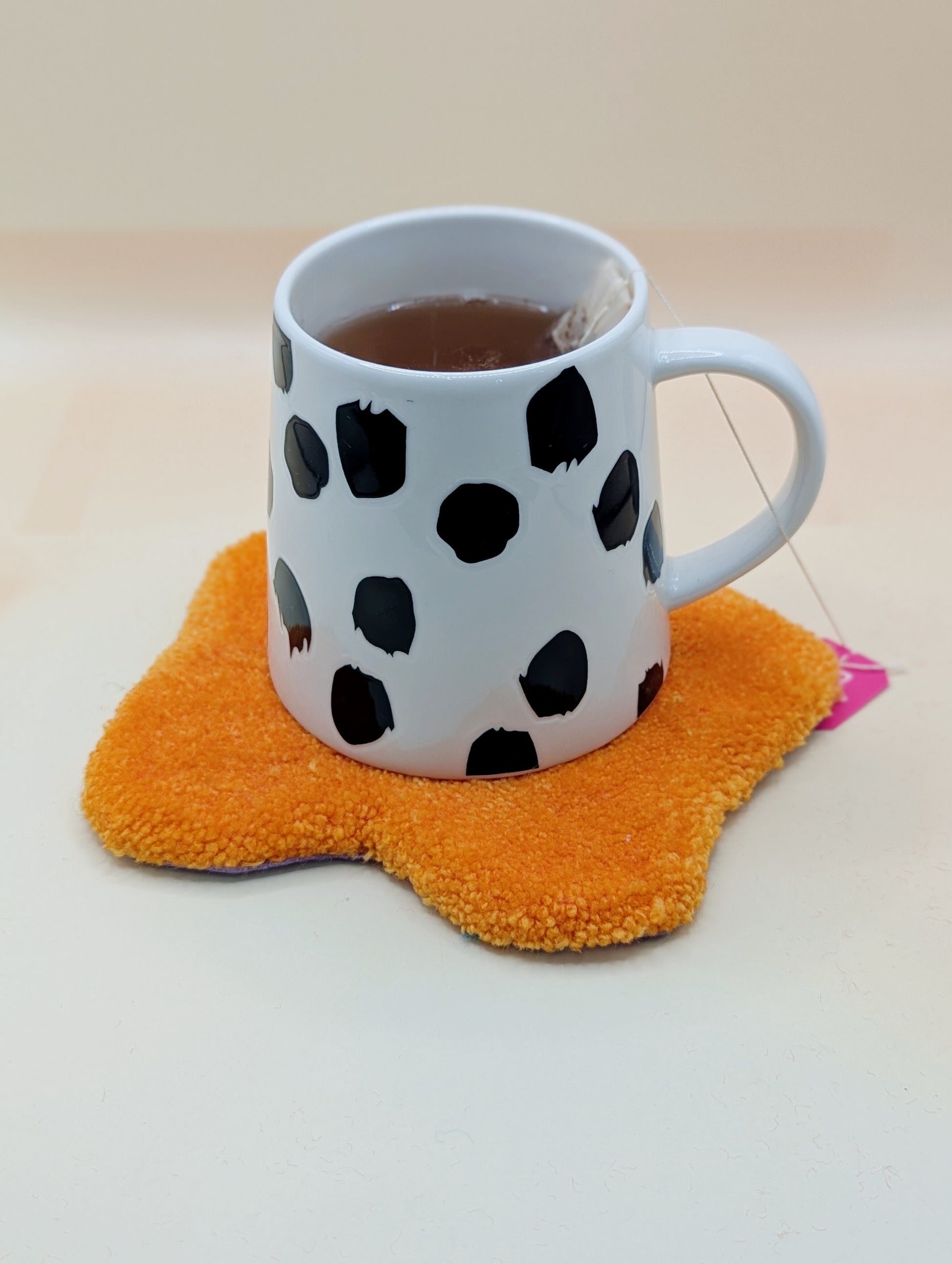 Soft tufted red and pink fried egg shaped mini rug/coaster with a mug of tea resting on it