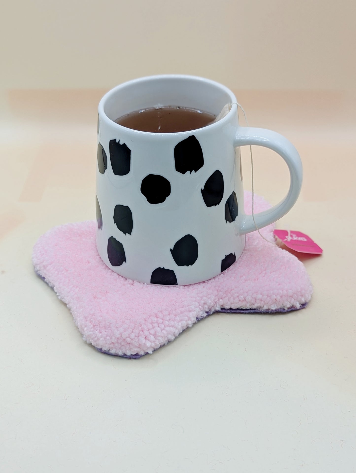Soft tufted pink and purple fried egg shaped mini rug/coaster with a mug of tea resting on it
