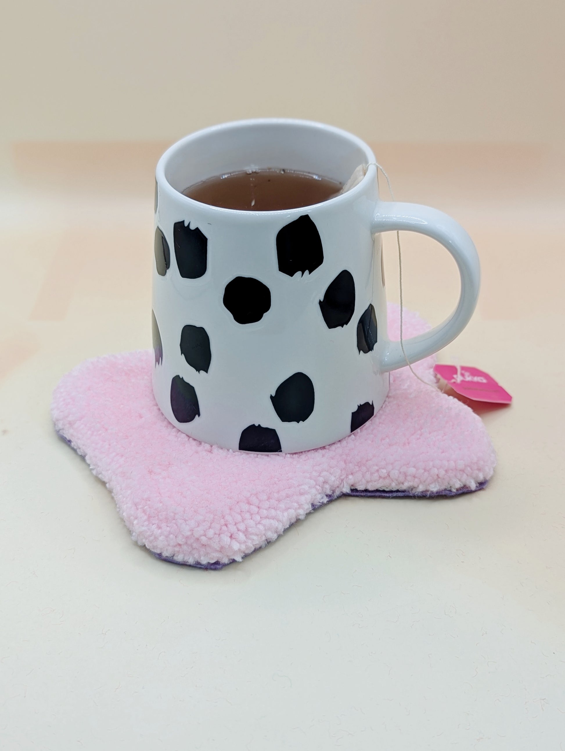 Soft tufted pink and purple fried egg shaped mini rug/coaster with a mug of tea resting on it