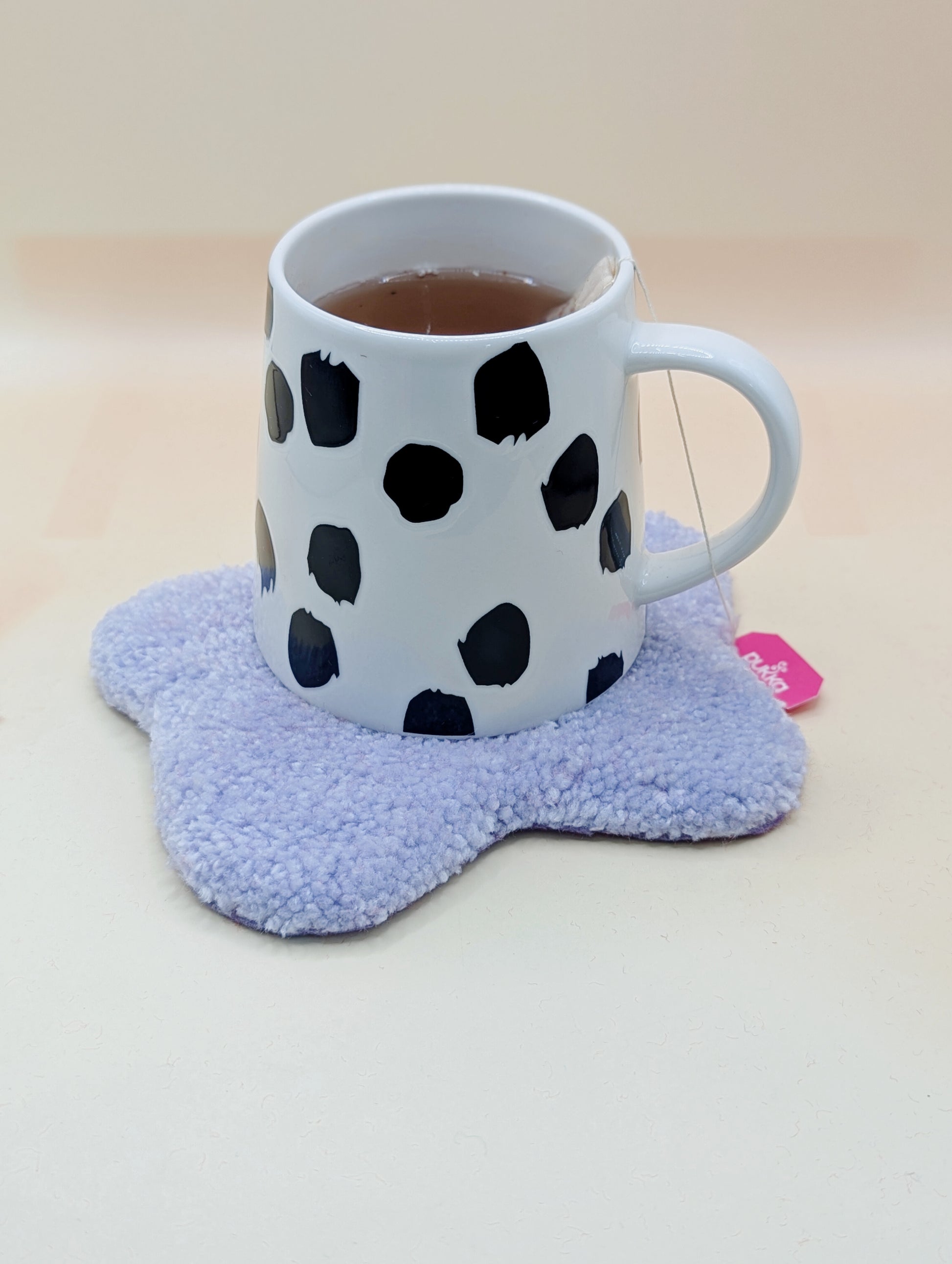 Soft tufted red and pink fried egg shaped mini rug/coaster with a mug of tea resting on it