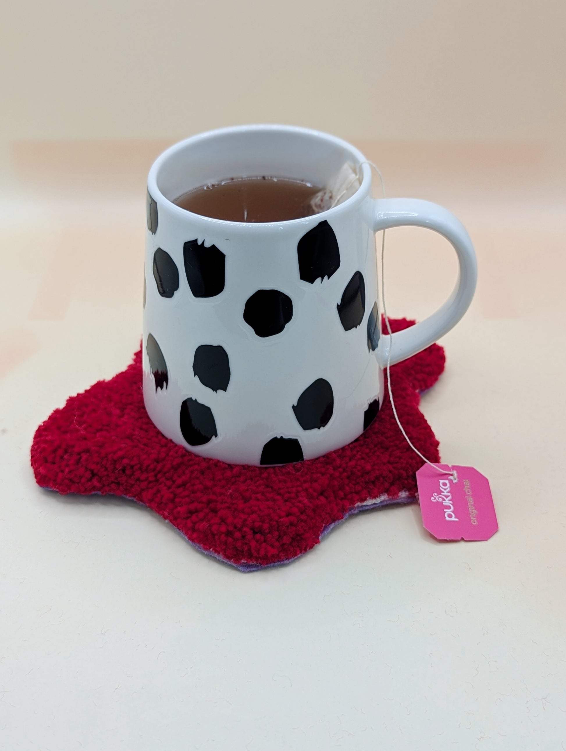 Soft tufted red and pink fried egg shaped mini rug/coaster with a mug of tea resting on it 