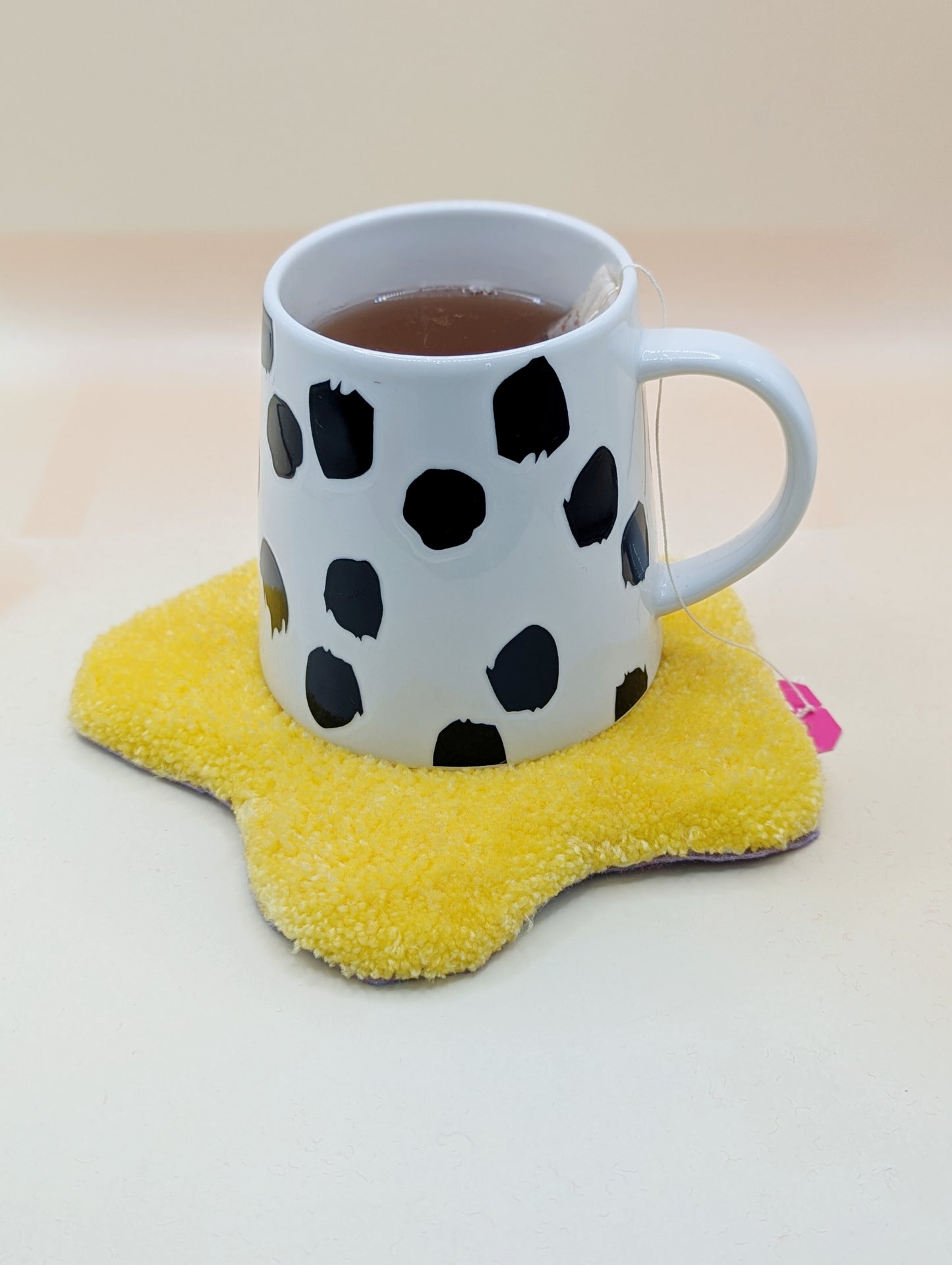 Soft tufted yellow and purple fried egg shaped mini rug/coaster with a mug of tea resting on it