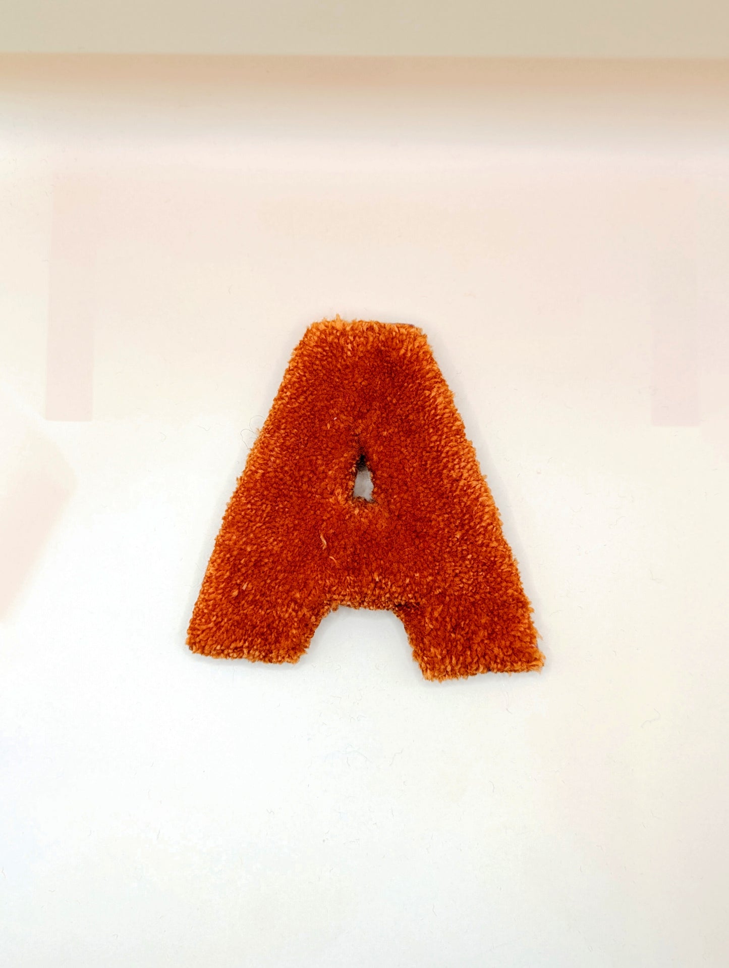 Soft tufted orange letter A with metal hook for easy hanging