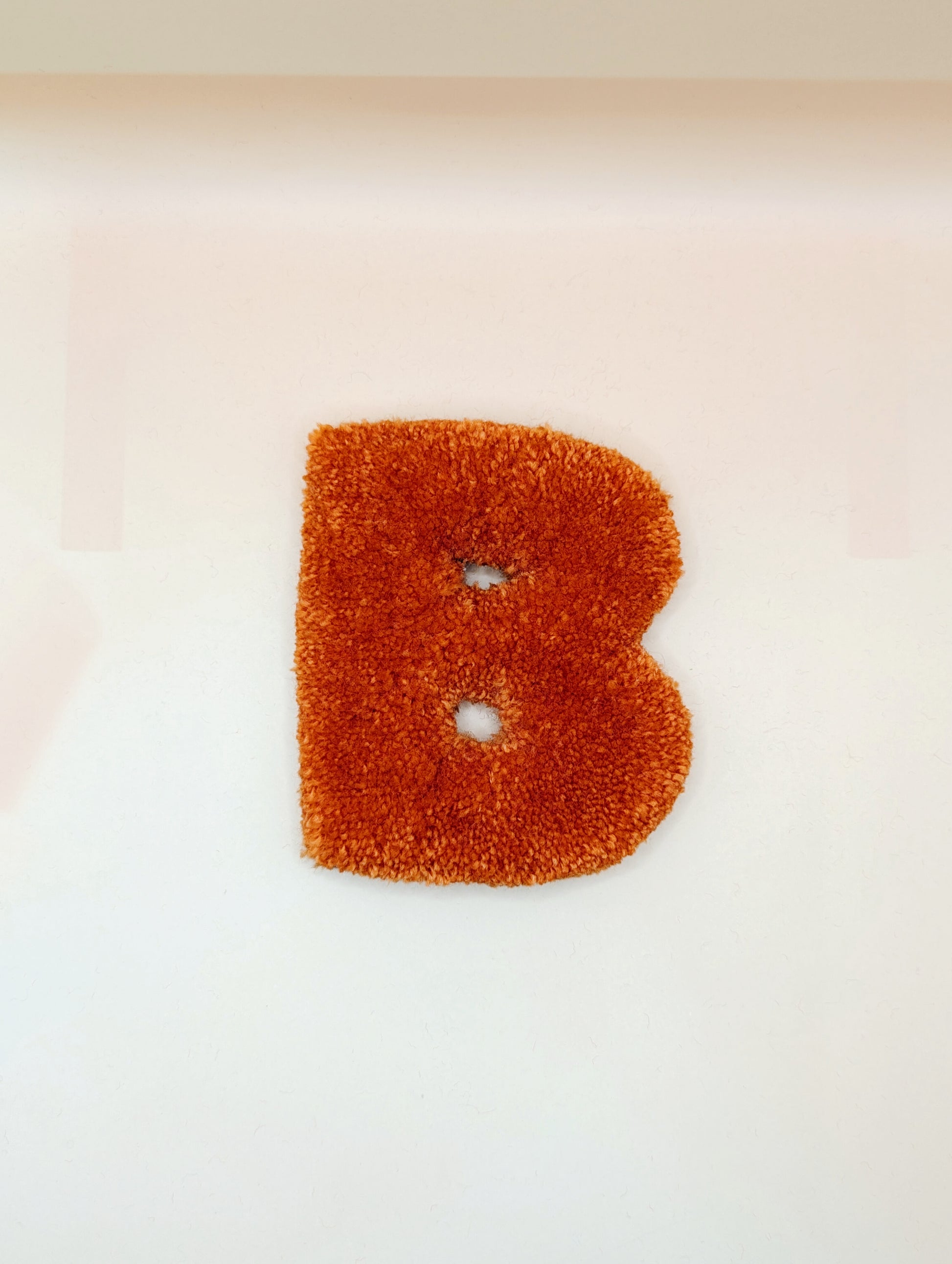 Soft tufted orange letter B with metal hook for easy hanging