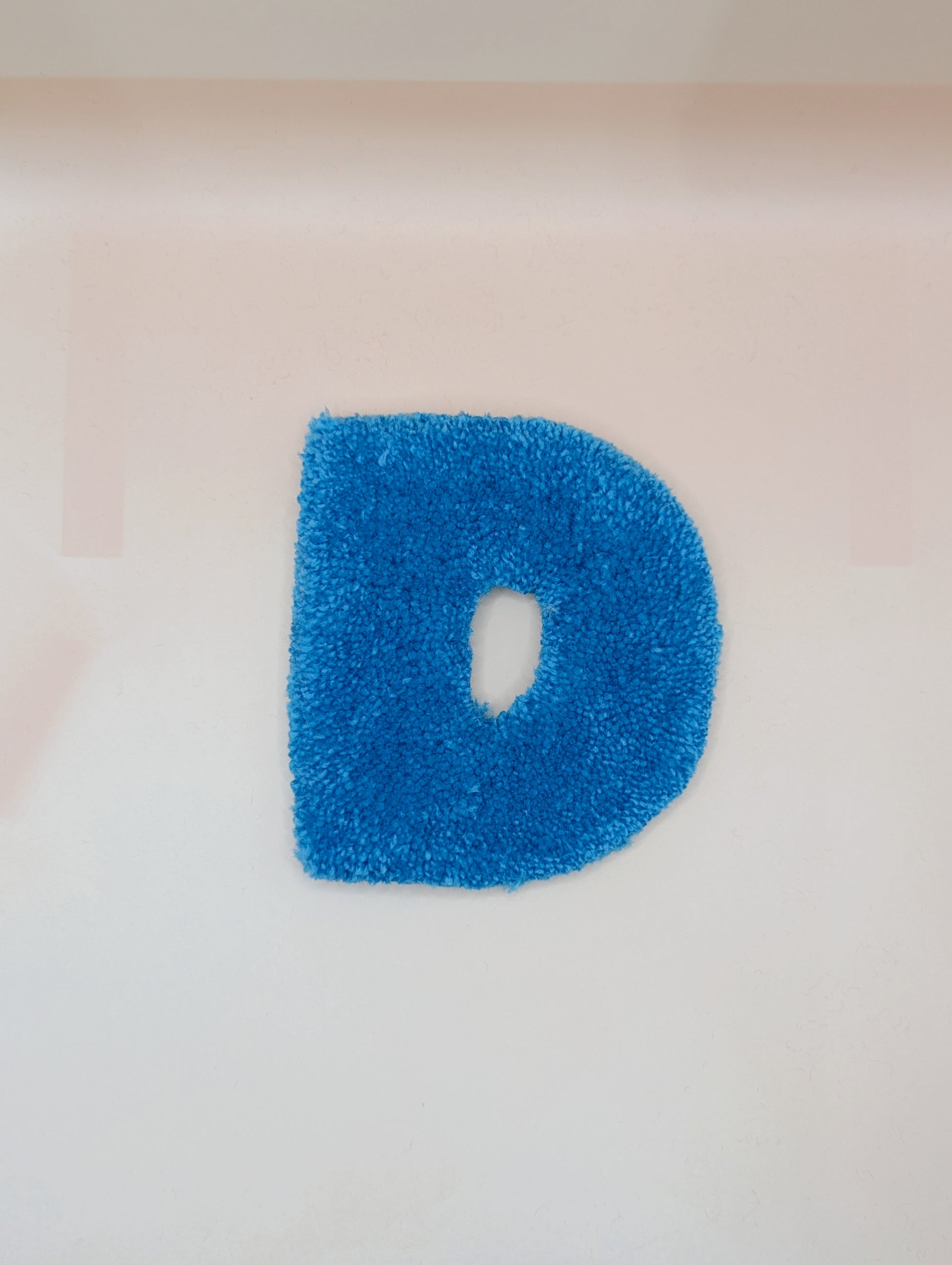 Soft tufted blue letter D with metal hook for easy hanging