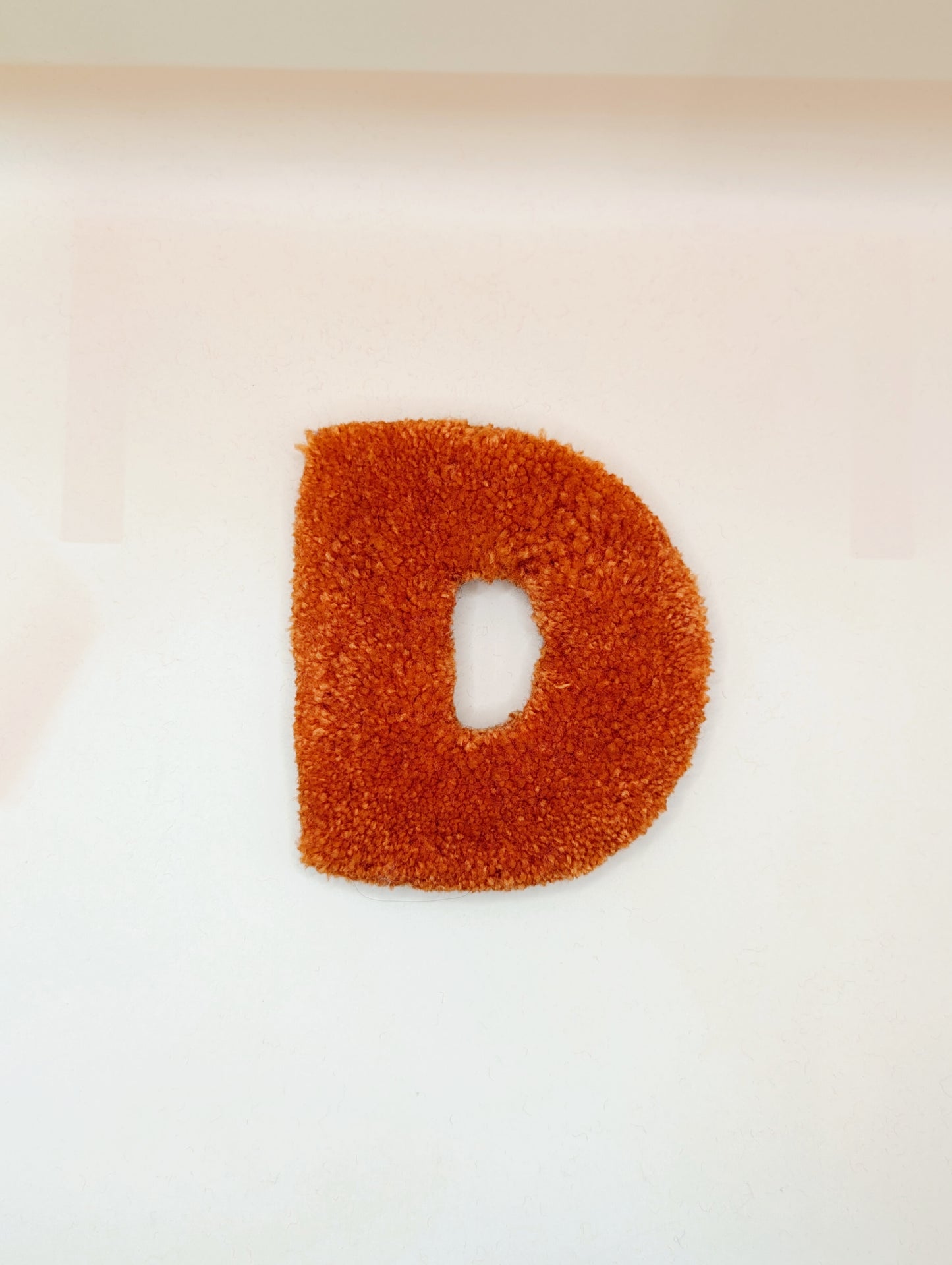 Soft tufted orange letter D with metal hook for easy hanging