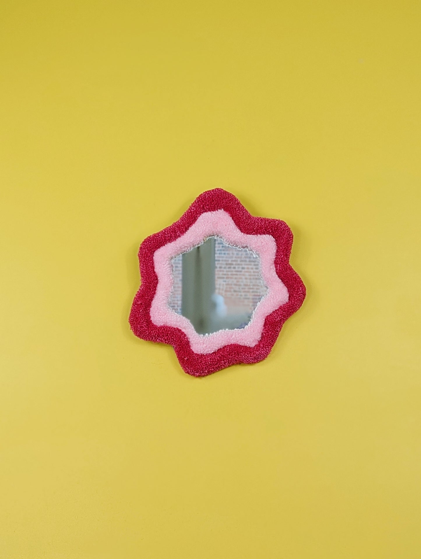 Handmade pink tufted mirror with organic wavy shape hanging on a yellow wall
