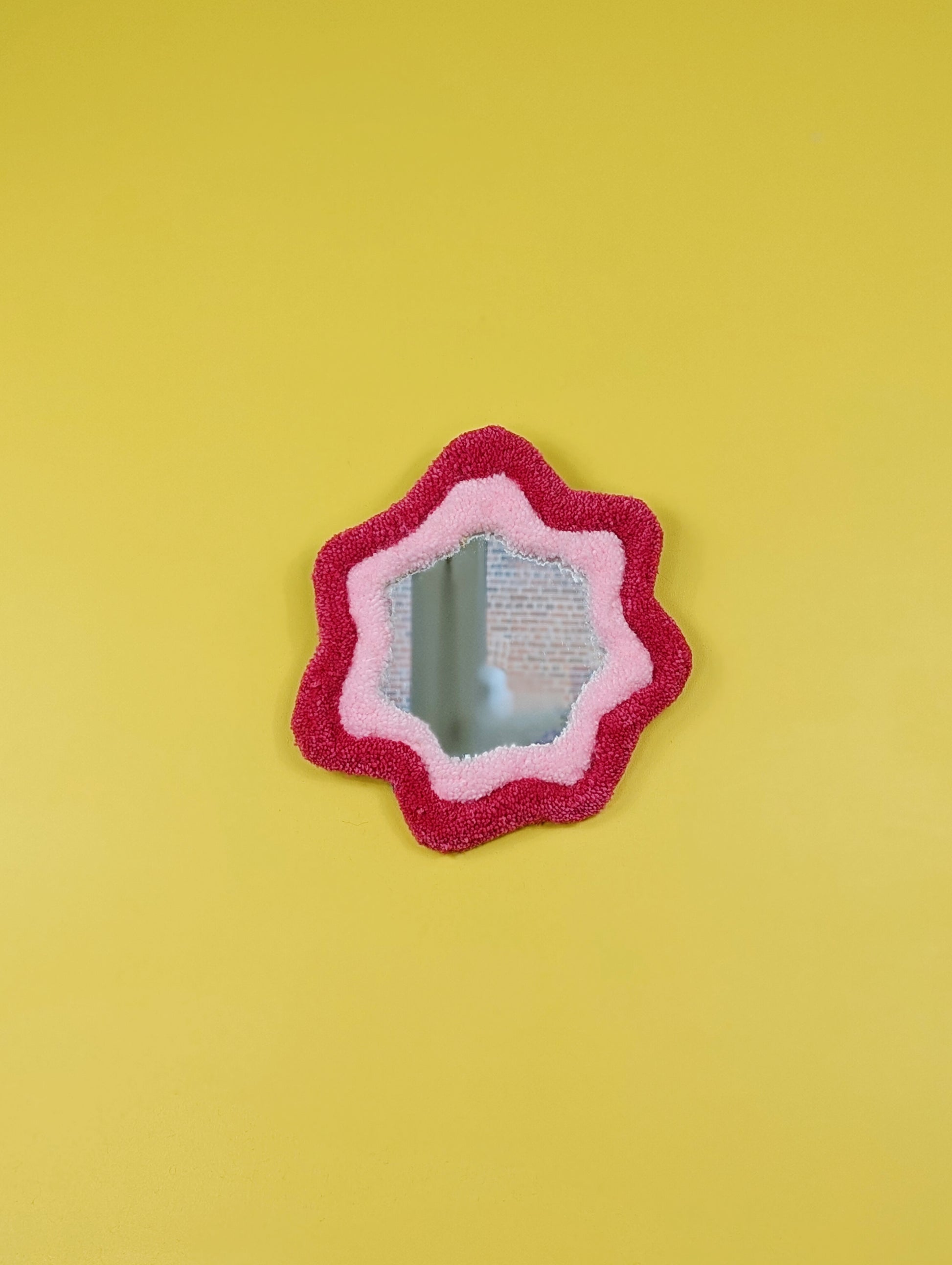Handmade pink tufted mirror with organic wavy shape hanging on a yellow wall