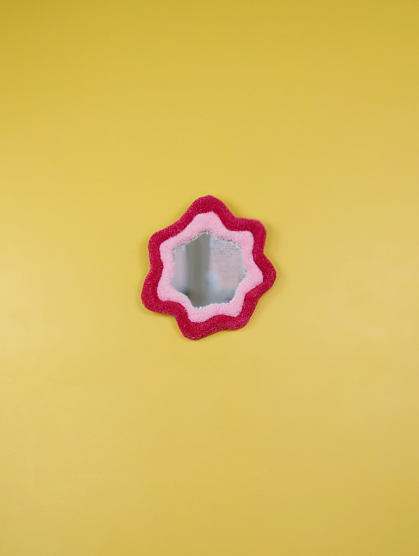 Handmade pink tufted mirror with organic wavy shape hanging on a yellow wall