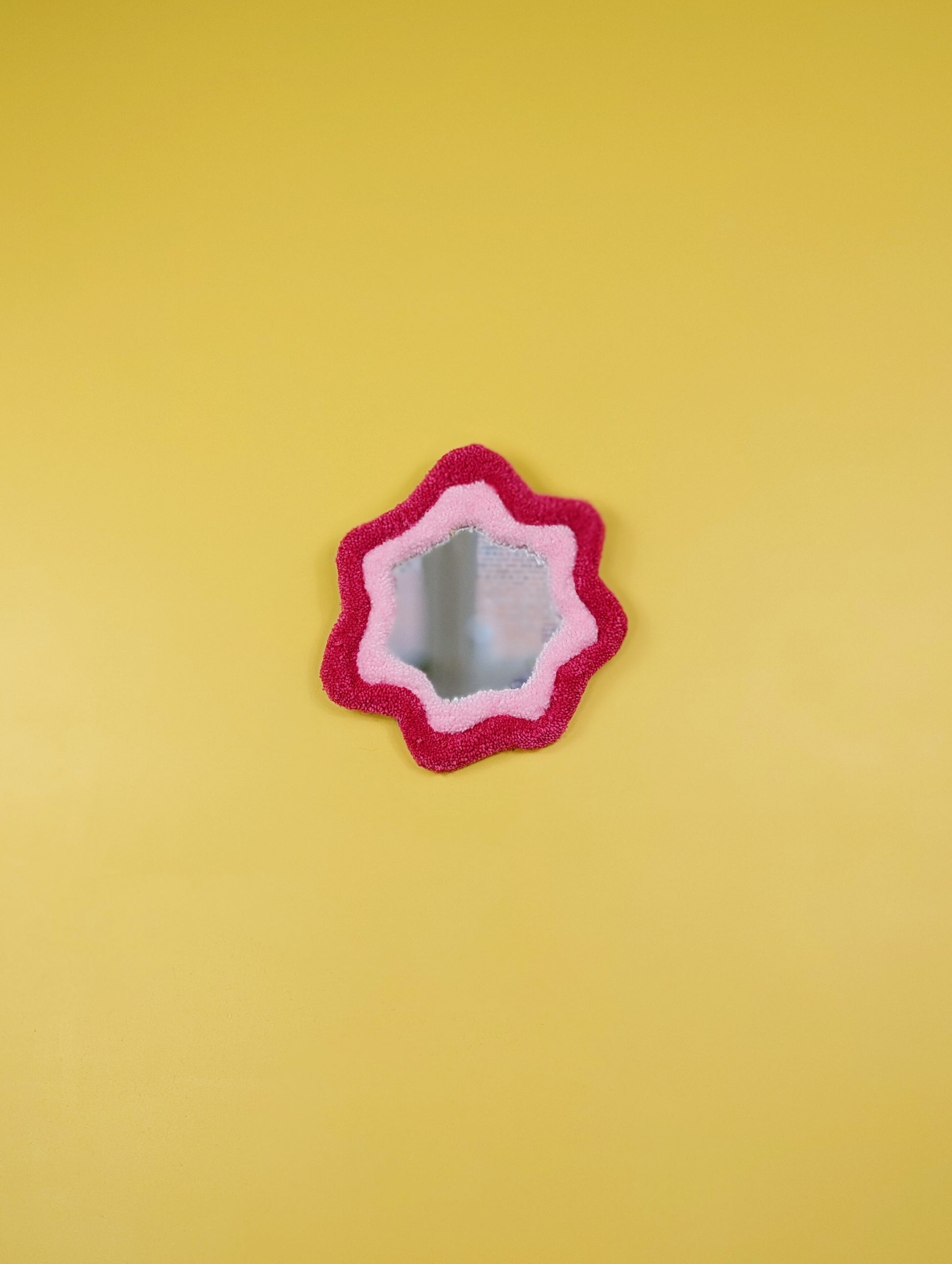 Handmade pink tufted mirror with organic wavy shape hanging on a yellow wall