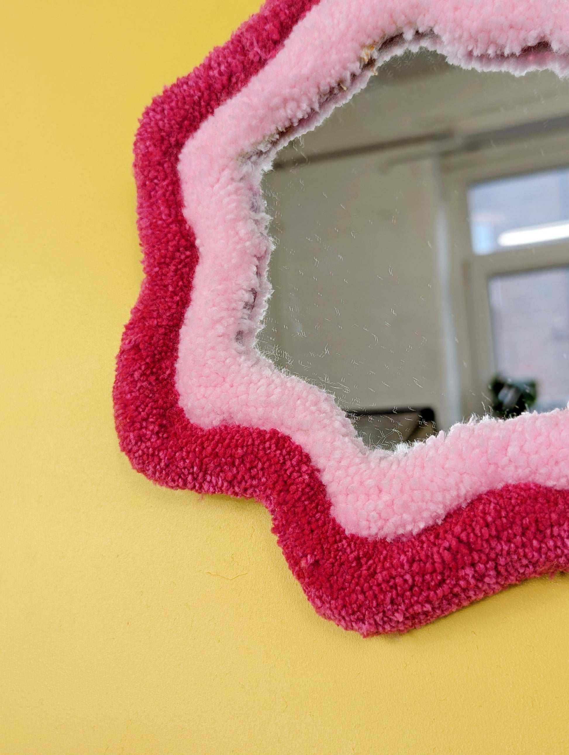 Handmade pink tufted mirror with organic wavy shape hanging on a yellow wall