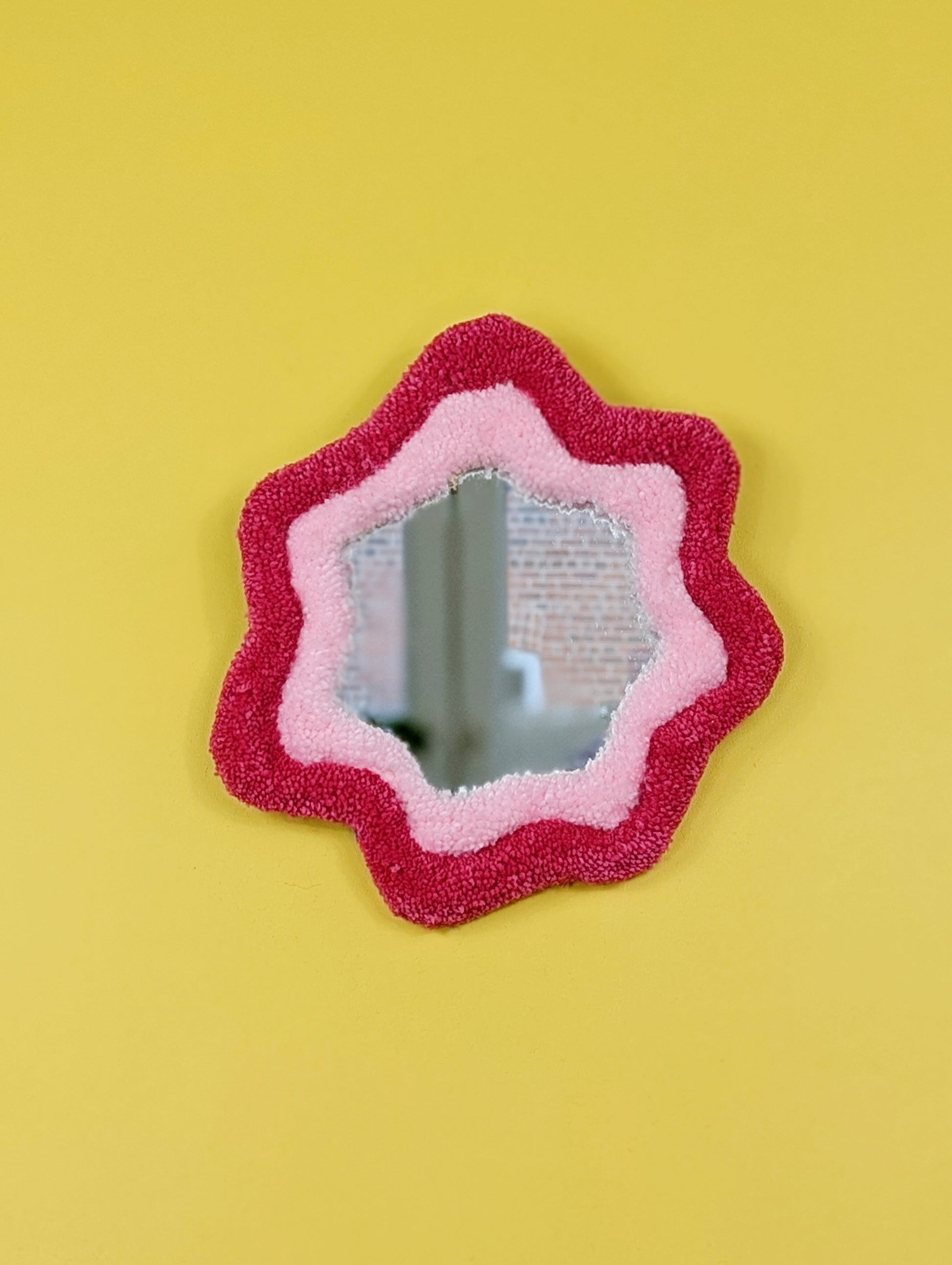 Handmade pink tufted mirror with organic wavy shape hanging on a yellow wall