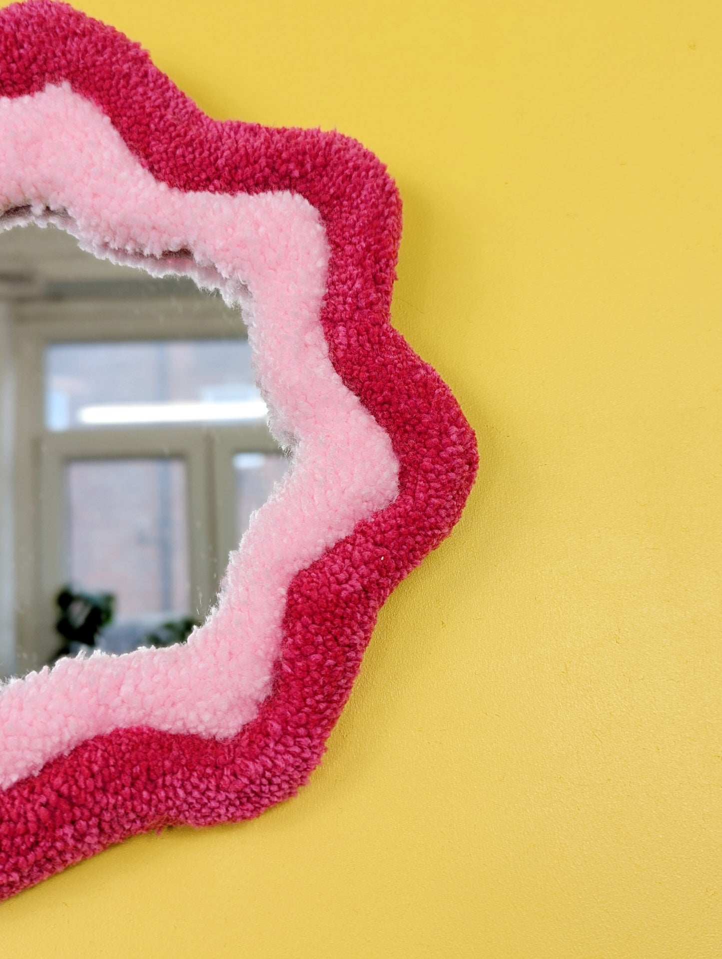 Handmade pink tufted mirror with organic wavy shape hanging on a yellow wall