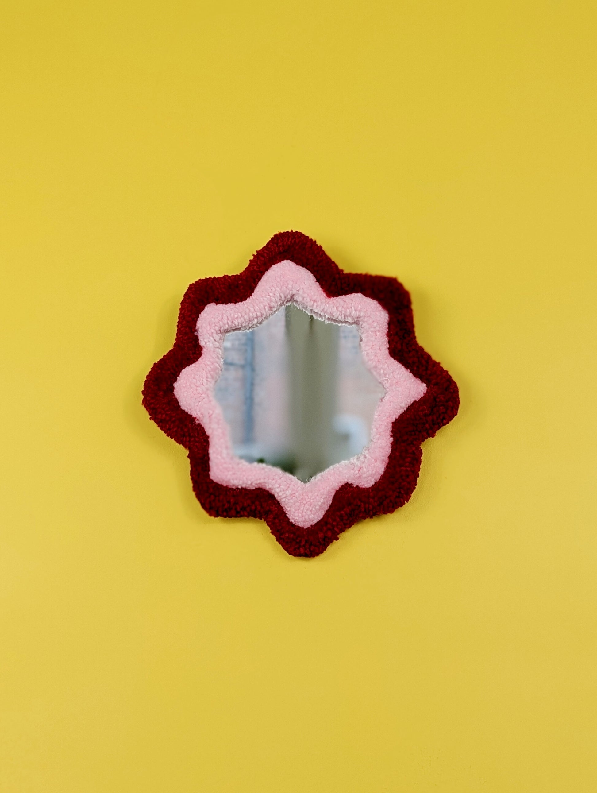  Handmade green and purple tufted mirror with organic wavy shape hanging on a yellow wall.