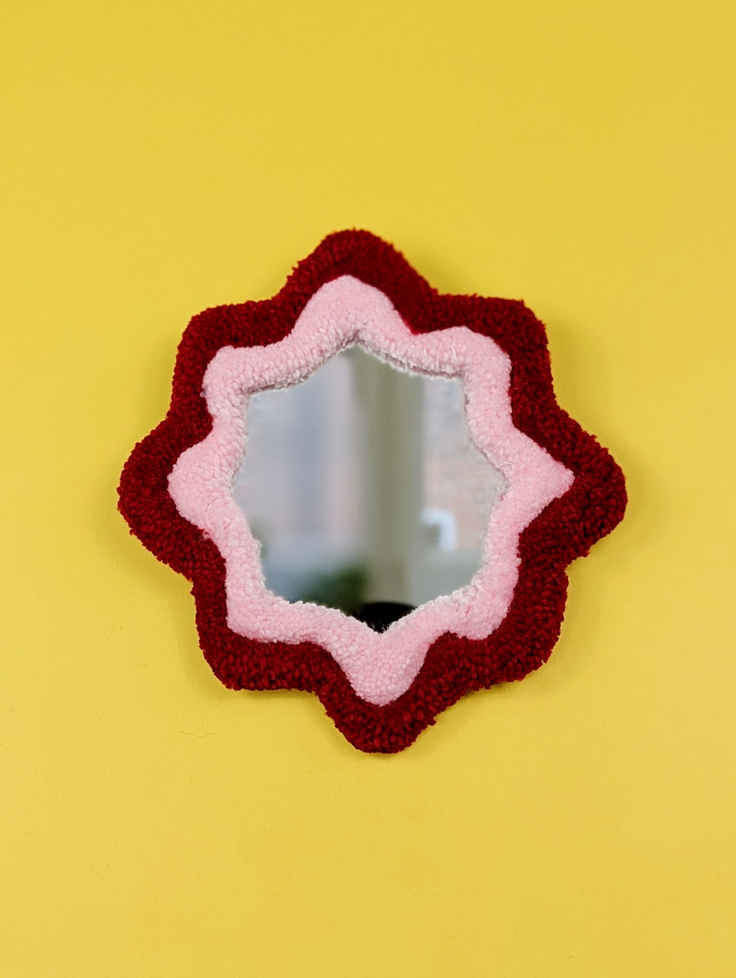  Handmade green and purple tufted mirror with organic wavy shape hanging on a yellow wall.