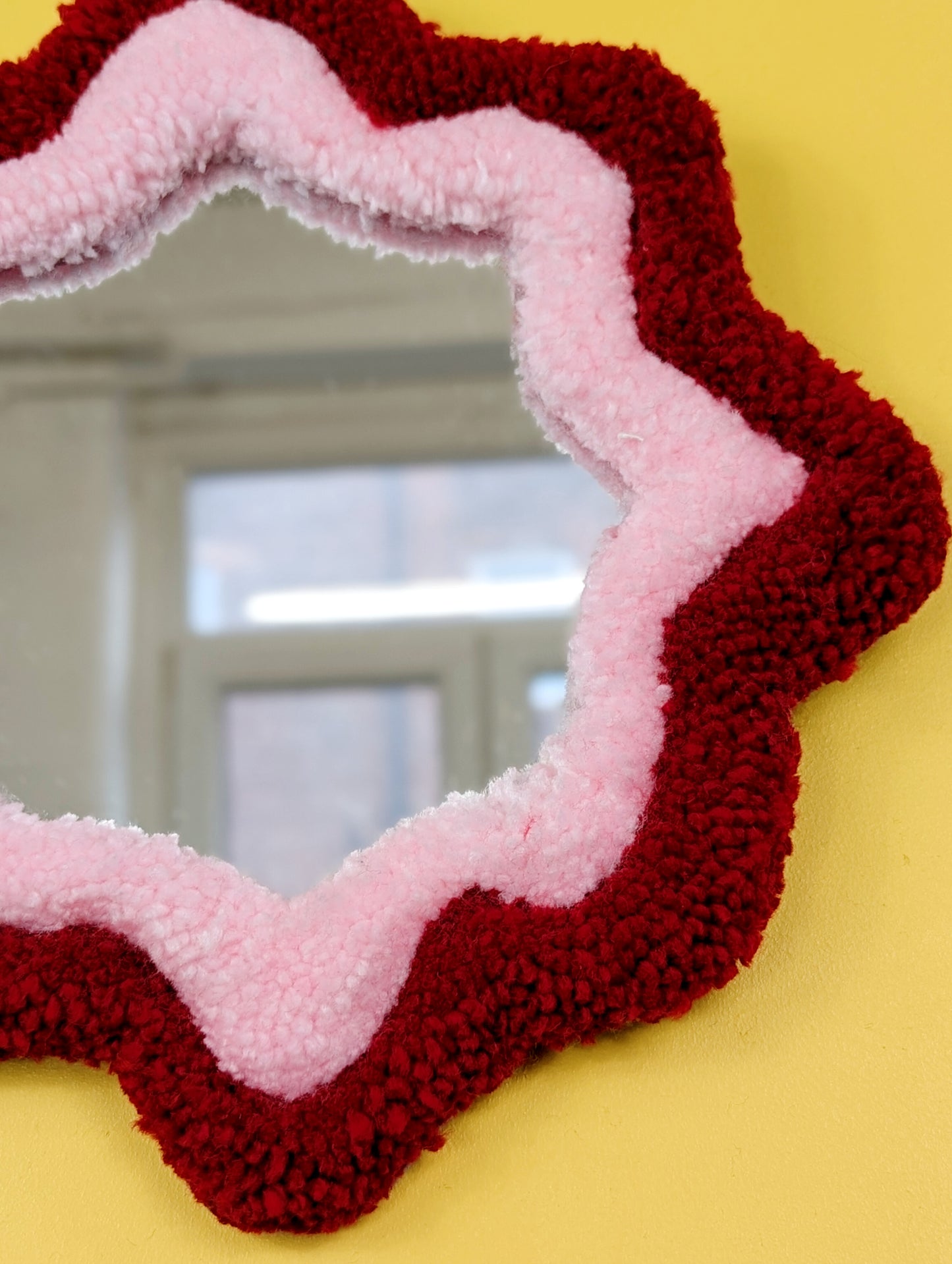  Handmade green and purple tufted mirror with organic wavy shape hanging on a yellow wall.