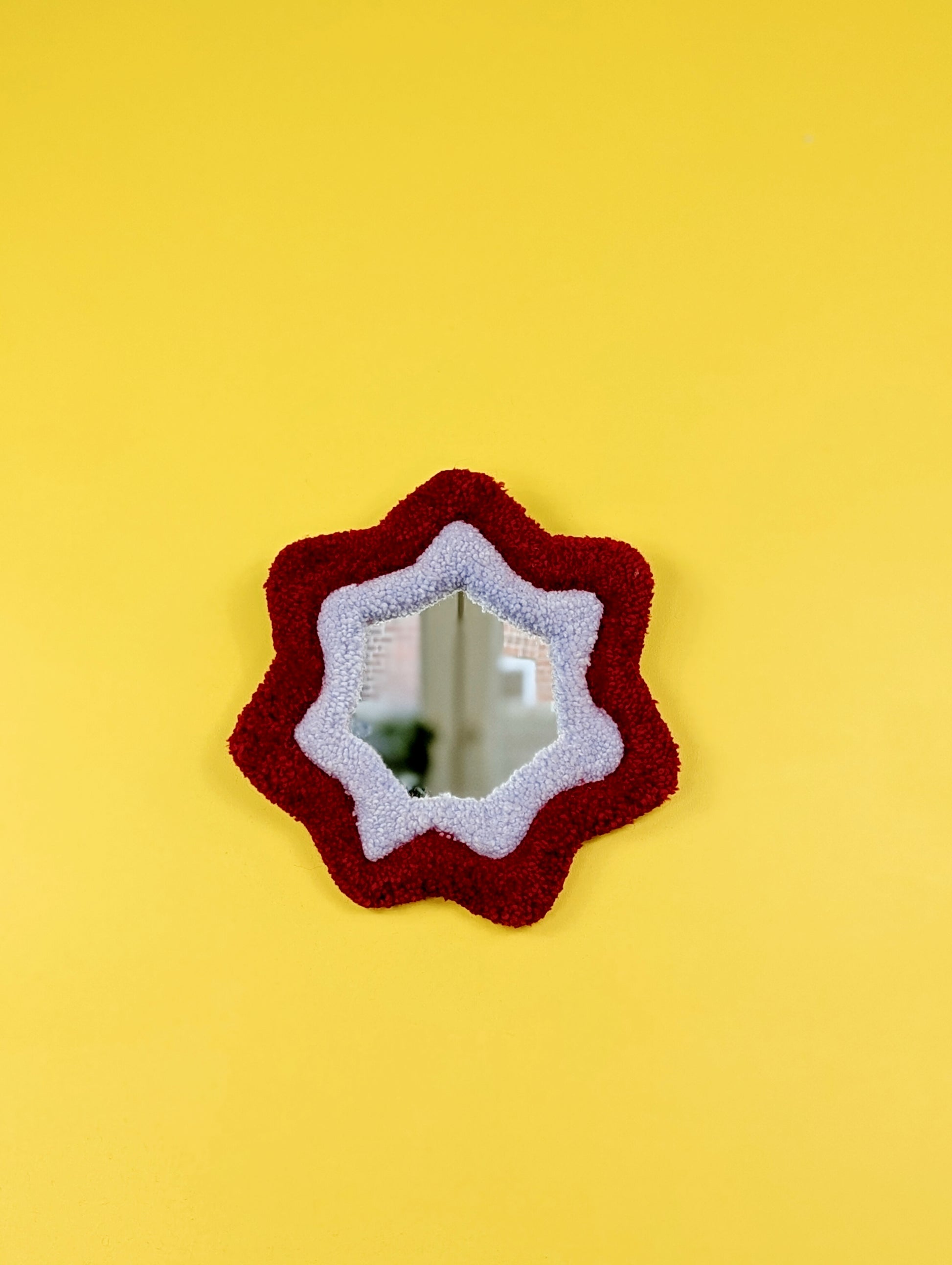  Handmade red and purple tufted mirror with organic wavy shape hanging on a yellow wall.