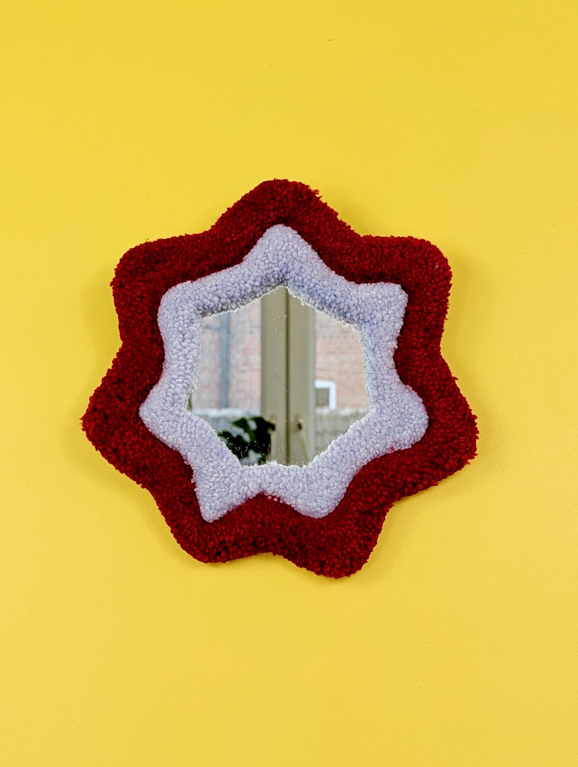  Handmade red and purple tufted mirror with organic wavy shape hanging on a yellow wall.