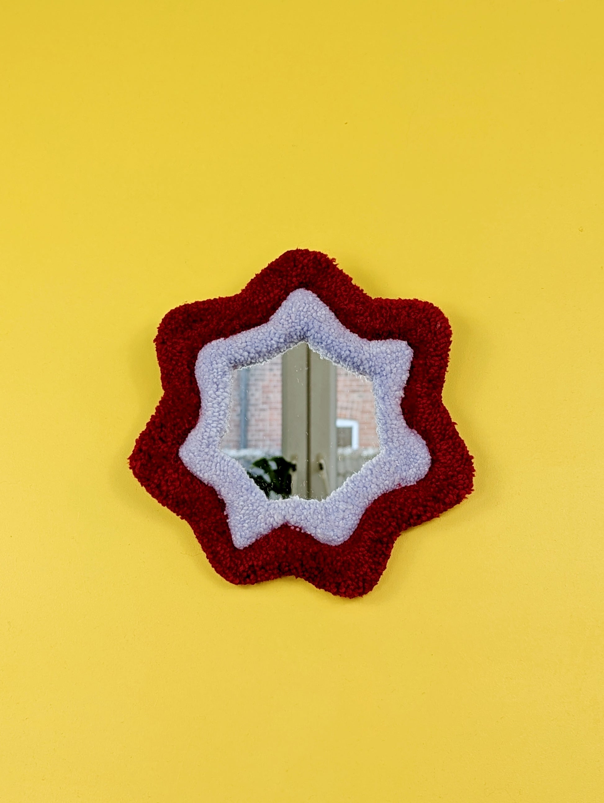  Handmade red and purple tufted mirror with organic wavy shape hanging on a yellow wall.