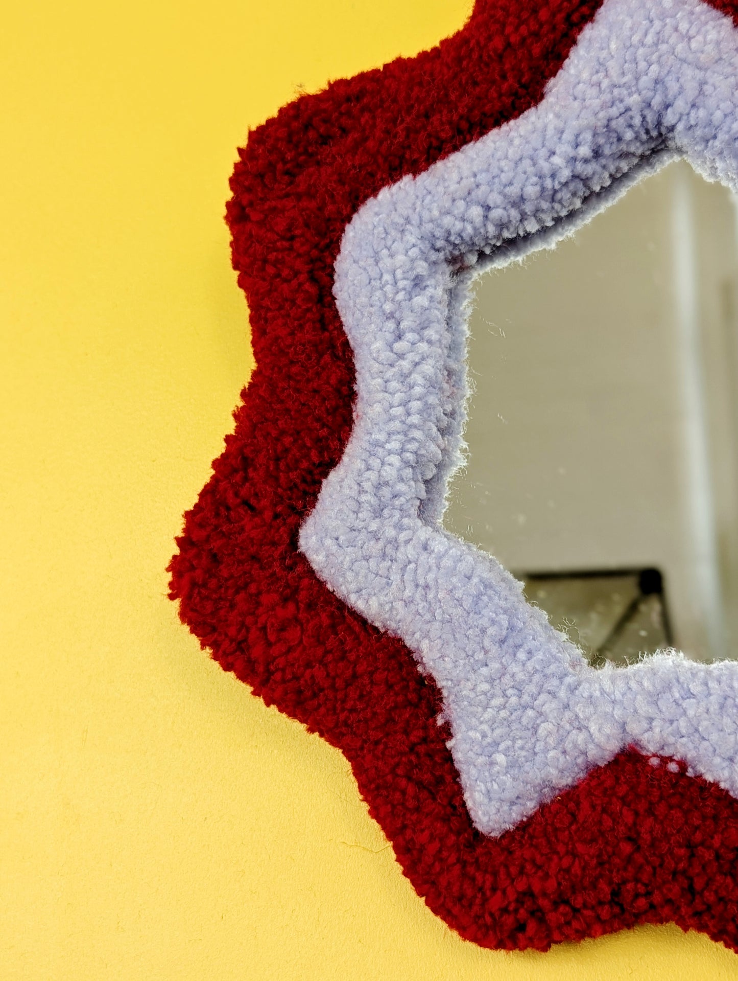  Handmade red and purple tufted mirror with organic wavy shape hanging on a yellow wall.