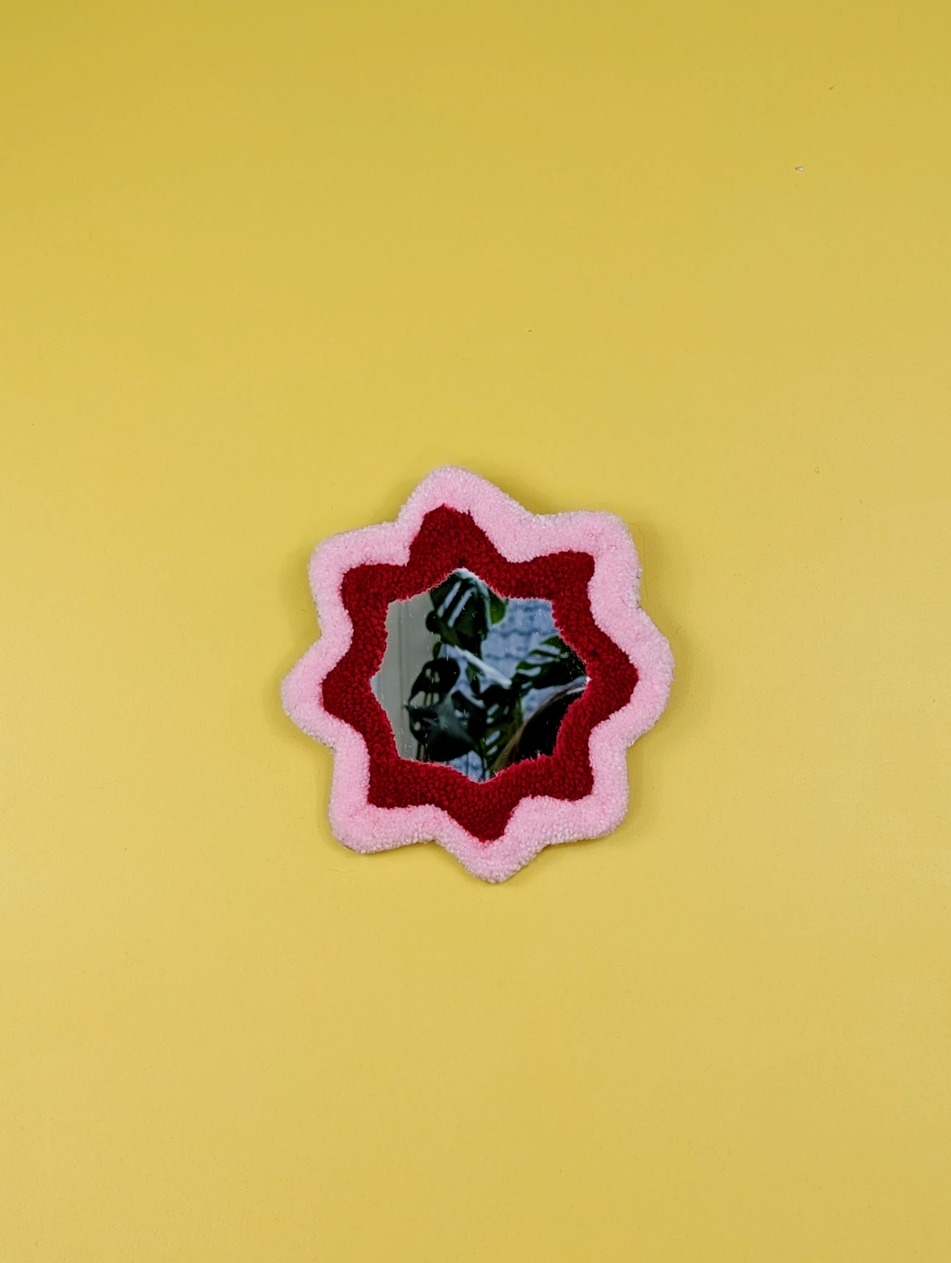  Handmade pink and red tufted mirror with organic wavy shape hanging on a yellow wall.