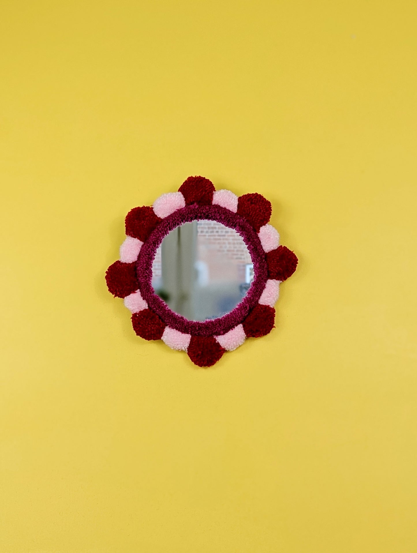 Handmade tufted petal mirror with red and pink textured yarn petals surrounding a round mirror