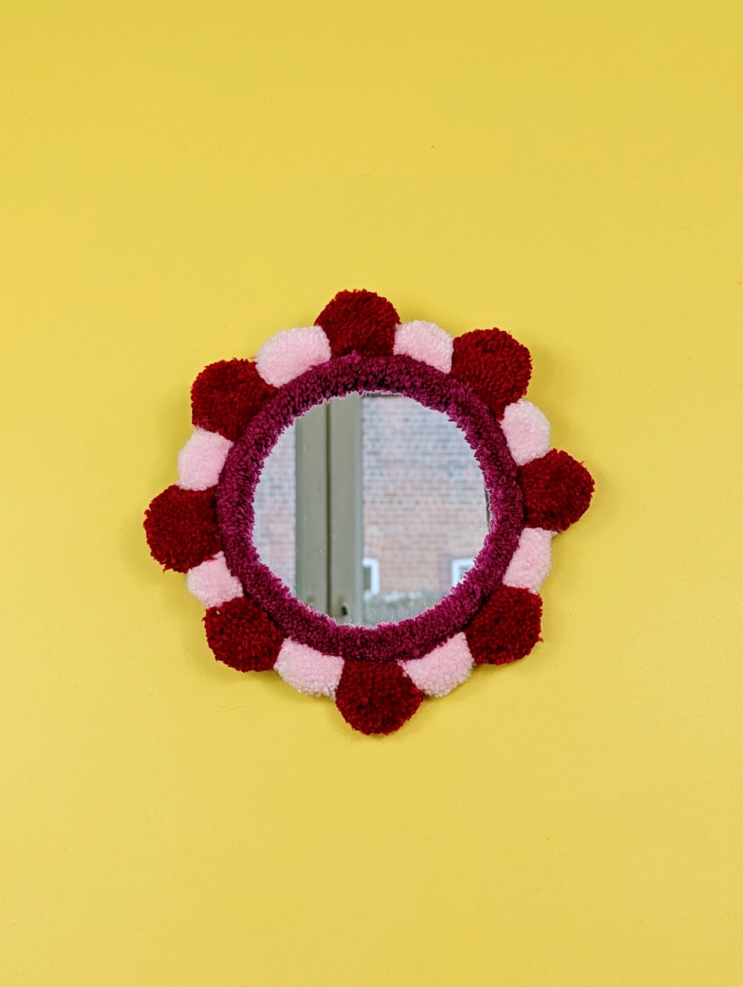 Handmade tufted petal mirror with red and pink textured yarn petals surrounding a round mirror