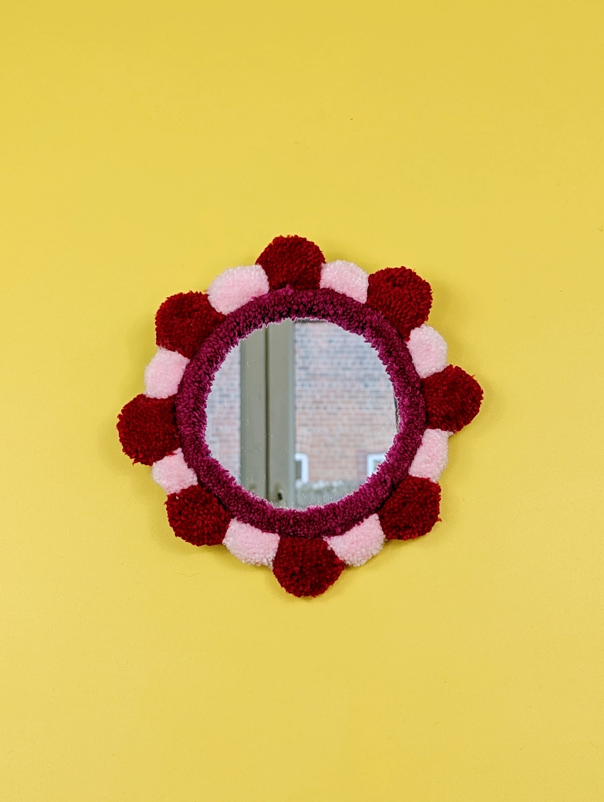 Handmade tufted petal mirror with red and pink textured yarn petals surrounding a round mirror