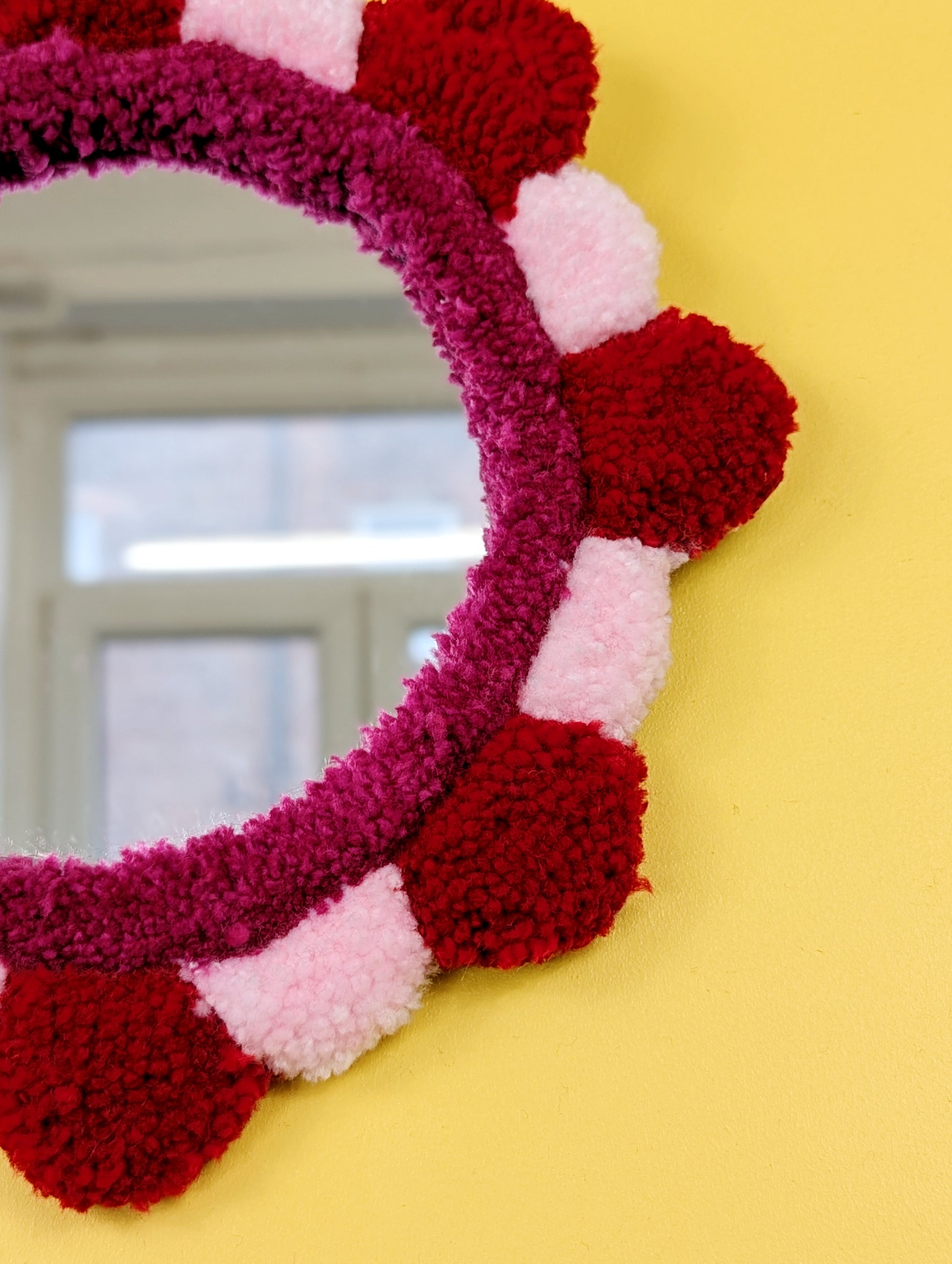Handmade tufted petal mirror with red and pink textured yarn petals surrounding a round mirror