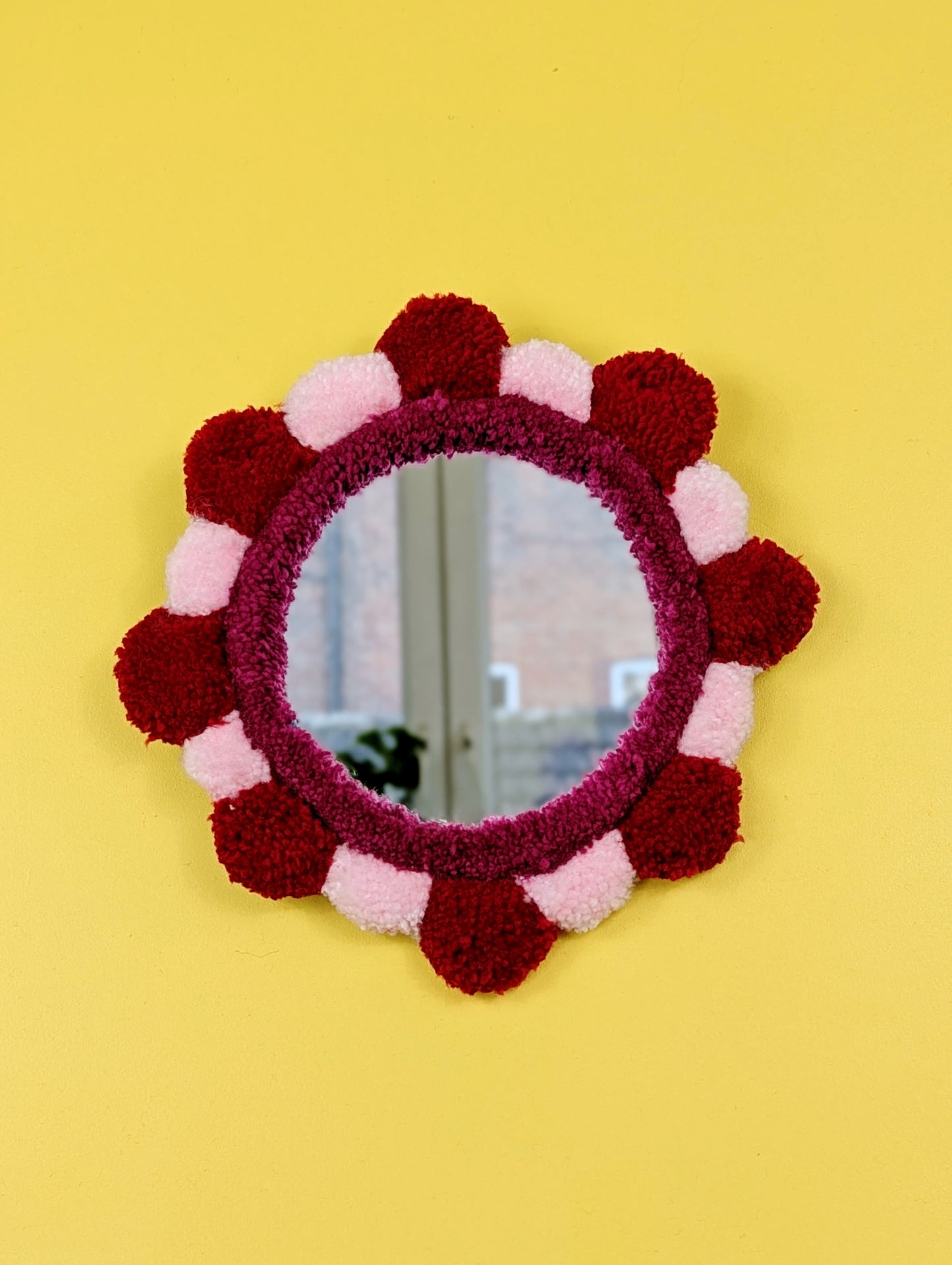 Handmade tufted petal mirror with red and pink textured yarn petals surrounding a round mirror