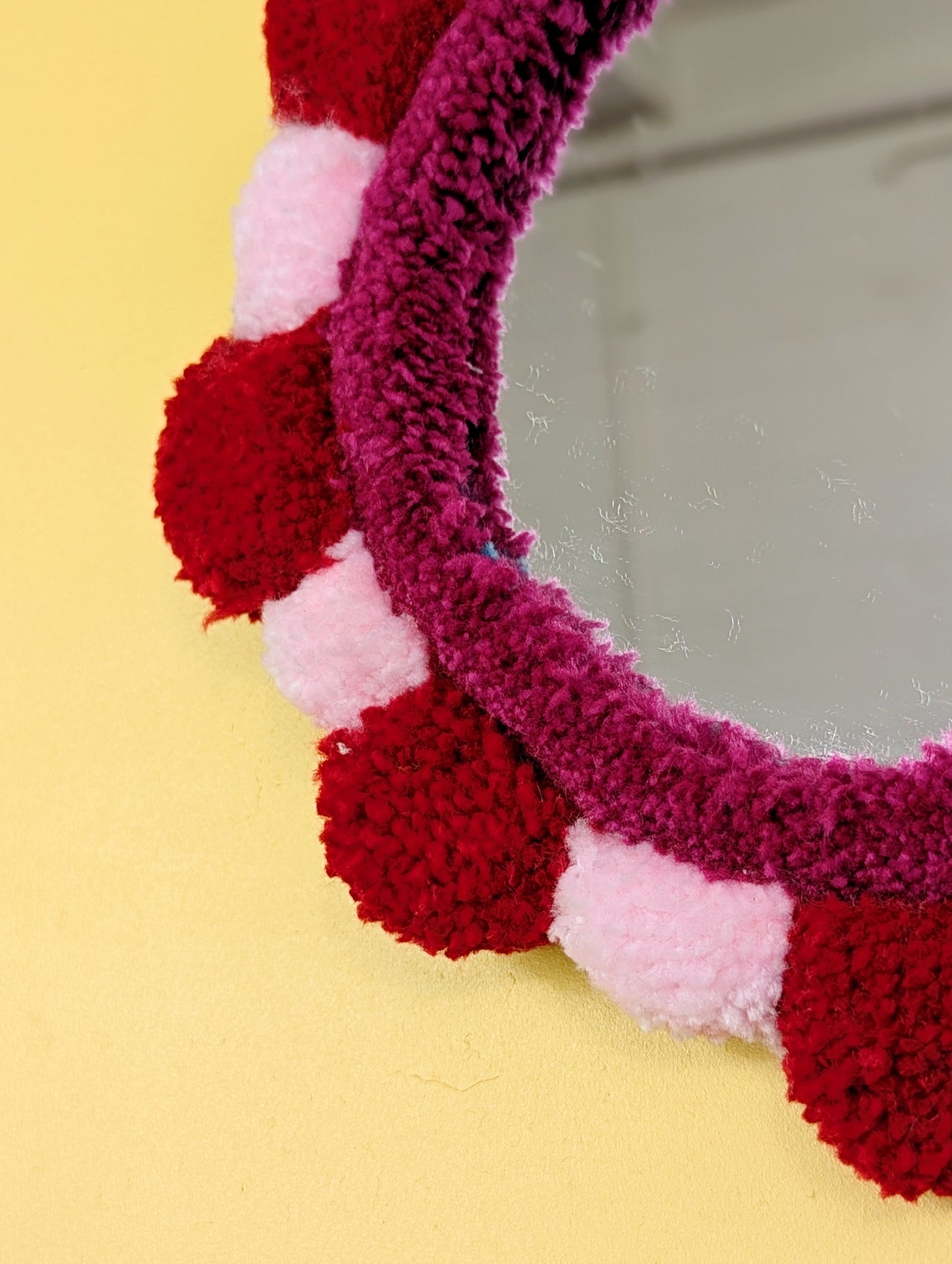 Handmade tufted petal mirror with red and pink textured yarn petals surrounding a round mirror