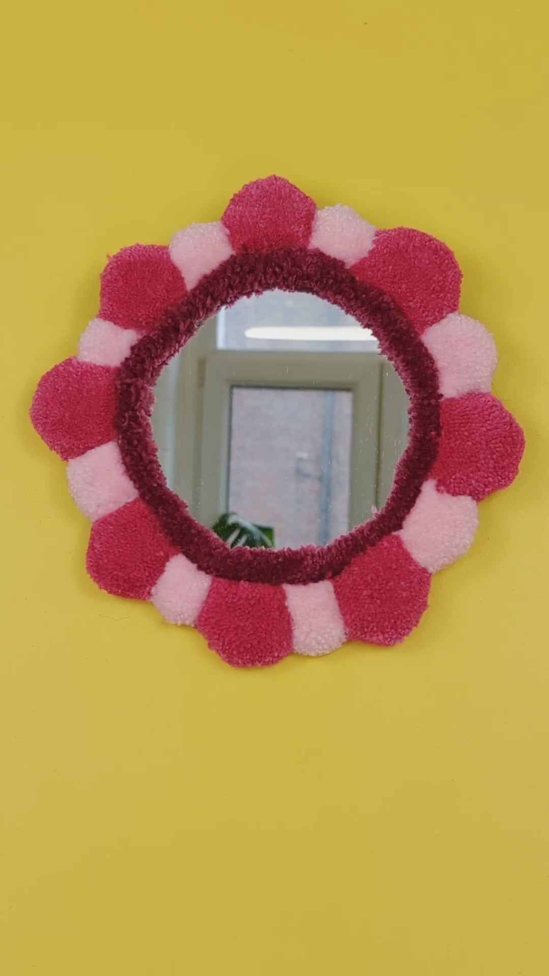 Handmade tufted petal mirror with pink textured yarn petals surrounding a round mirror