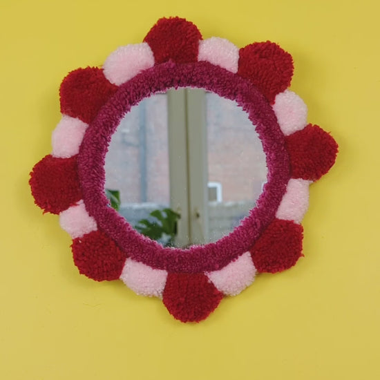 Handmade tufted petal mirror with red and pink textured yarn petals surrounding a round mirror