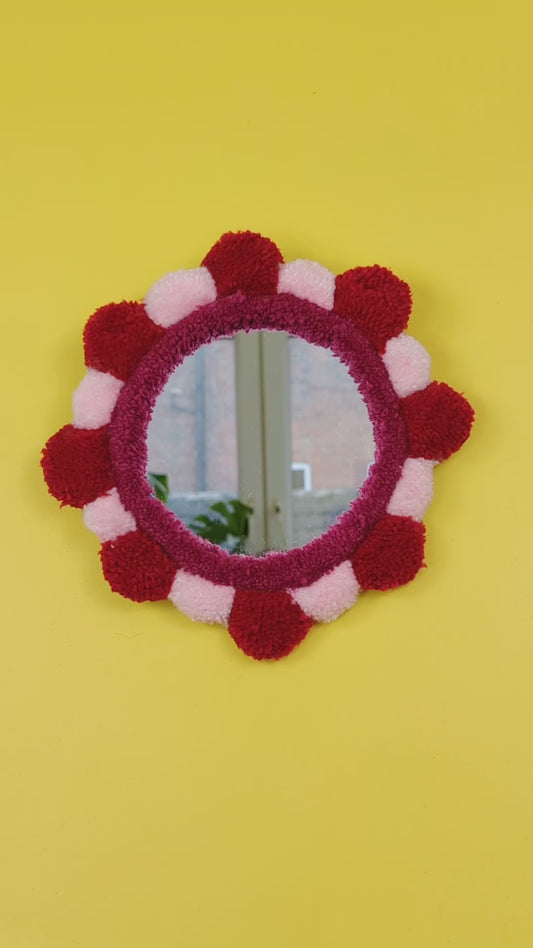 Handmade tufted petal mirror with red and pink textured yarn petals surrounding a round mirror