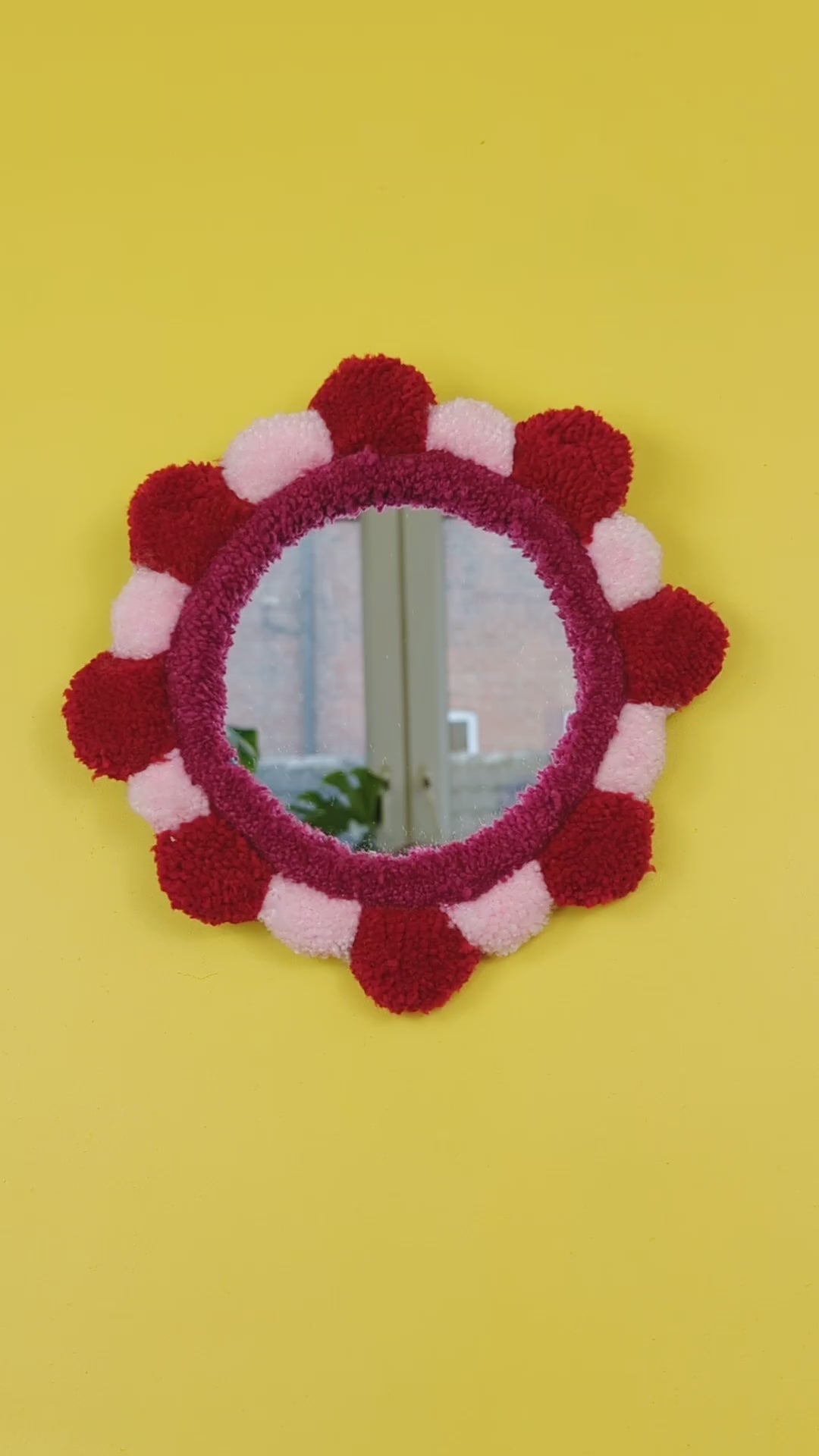 Handmade tufted petal mirror with red and pink textured yarn petals surrounding a round mirror