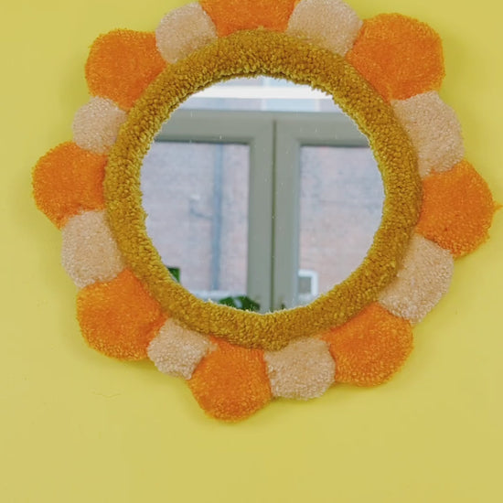 Handmade tufted petal mirror with alternating orange and beige textured yarn petals surrounding a round mirror