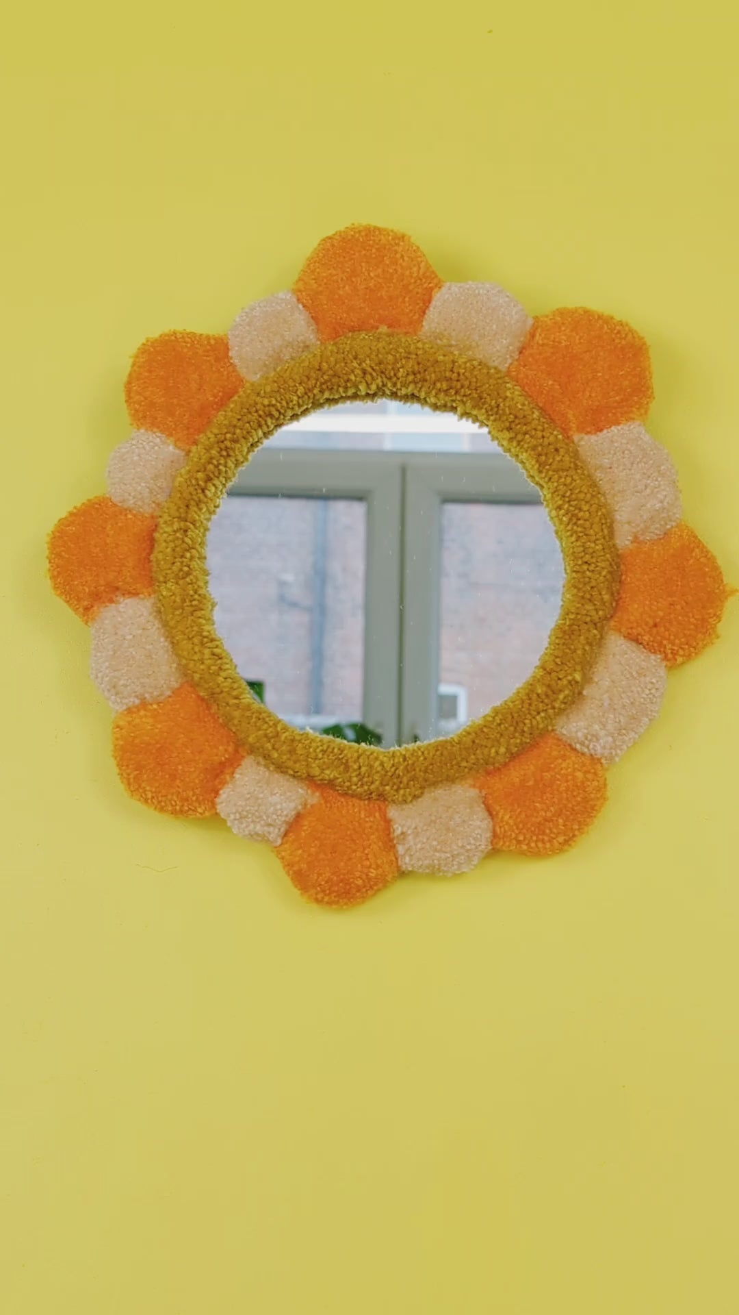 Handmade tufted petal mirror with alternating orange and beige textured yarn petals surrounding a round mirror