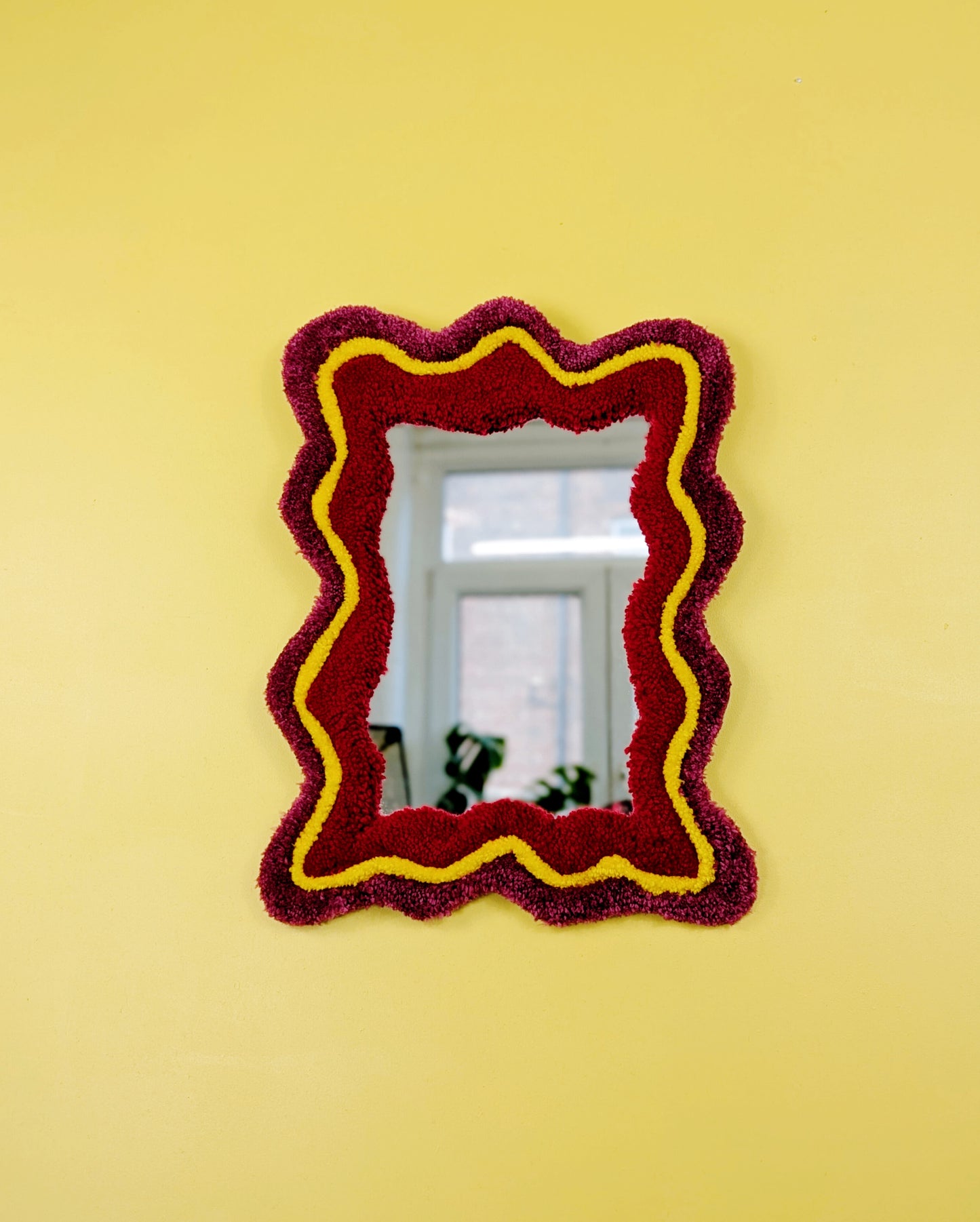 Handmade wavy tufted mirror with colourful textured frame in dark pink, bright yellow and red, modern aesthetic wall décor for home interiors.