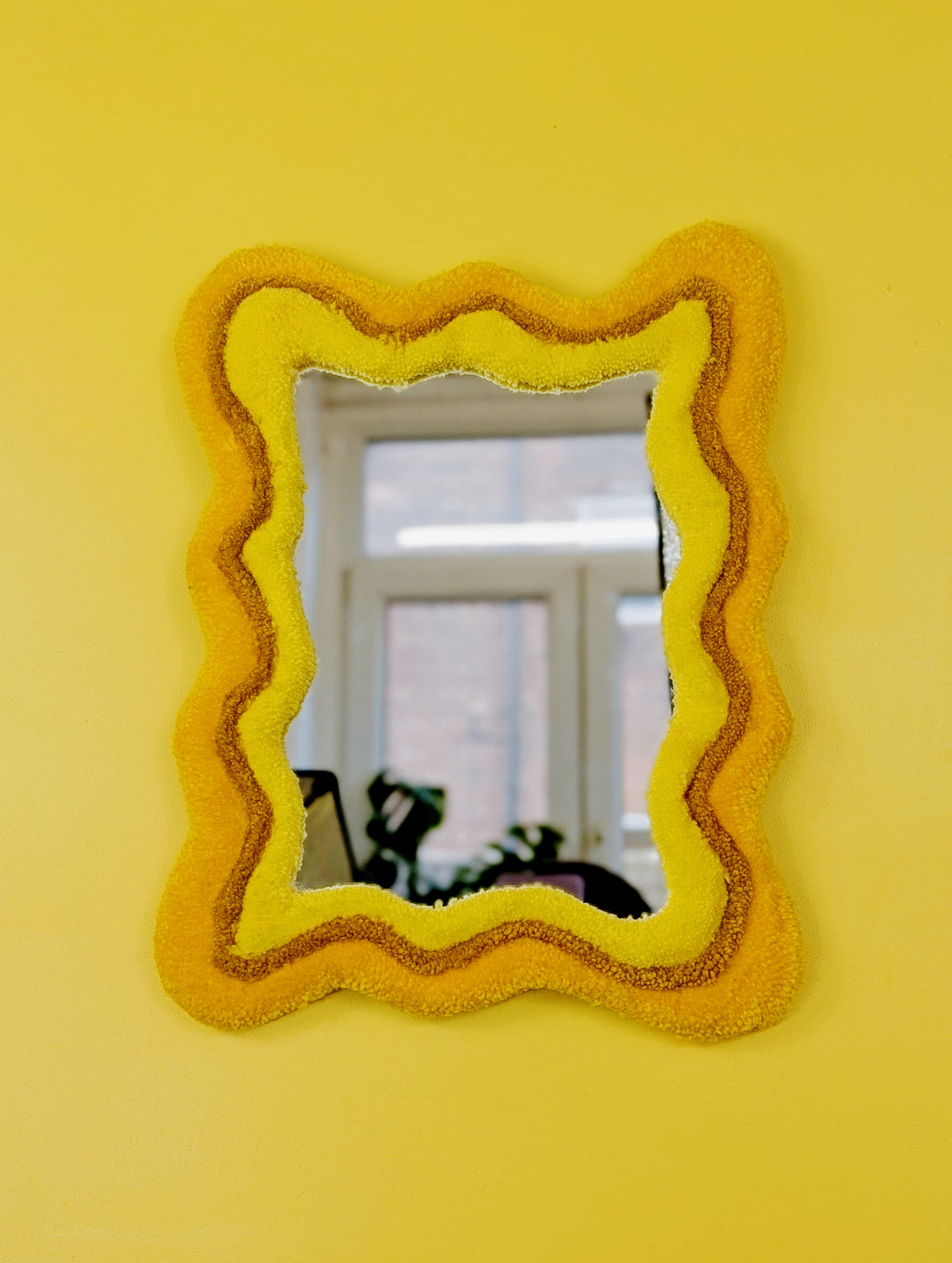 Handmade wavy tufted mirror with colourful textured frame in alternating shades of sunshine yellow, mustard yellow and bright yellow, modern aesthetic wall décor for home interiors.