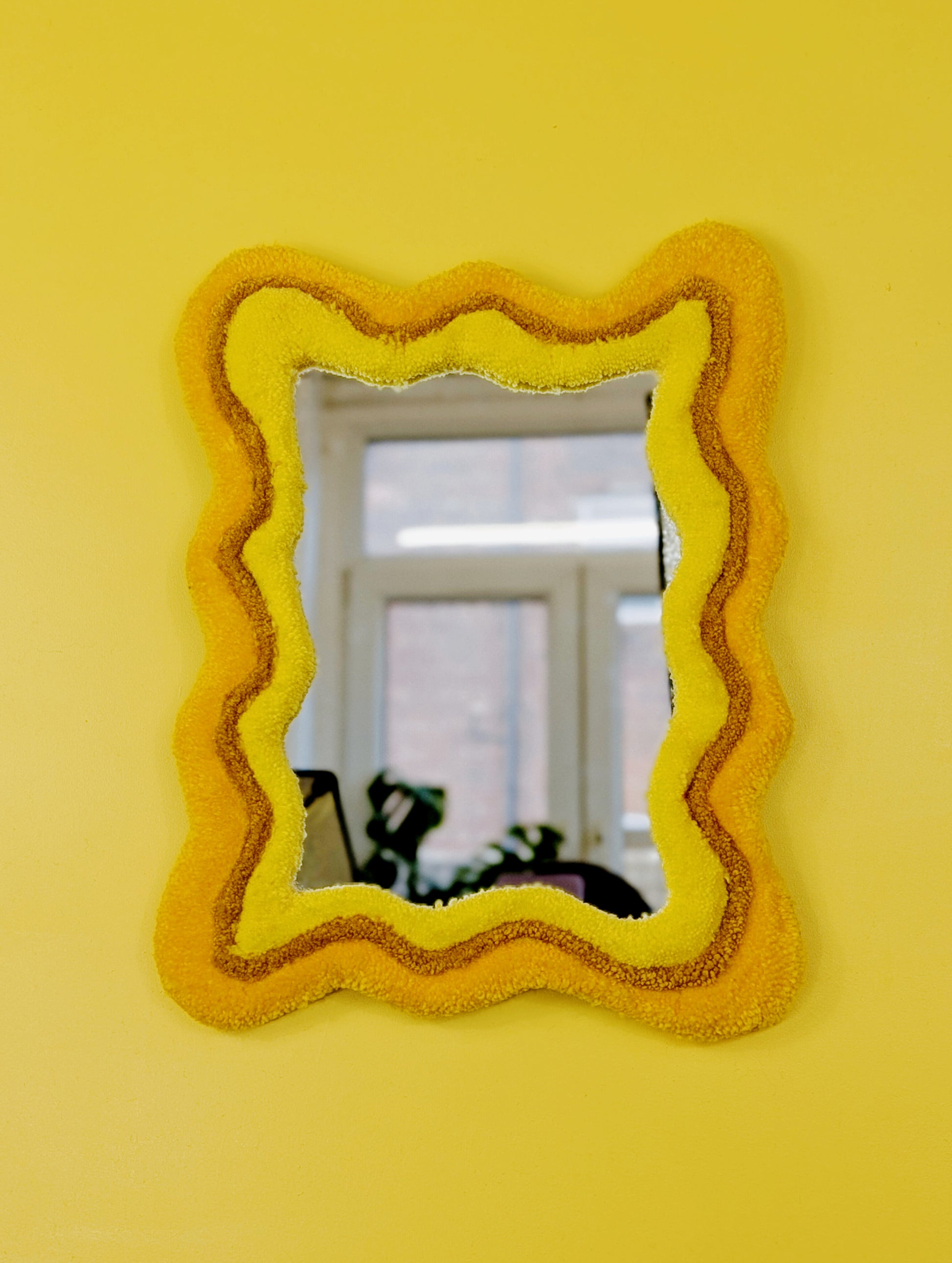 Handmade wavy tufted mirror with colourful textured frame in alternating shades of sunshine yellow, mustard yellow and bright yellow, modern aesthetic wall décor for home interiors.