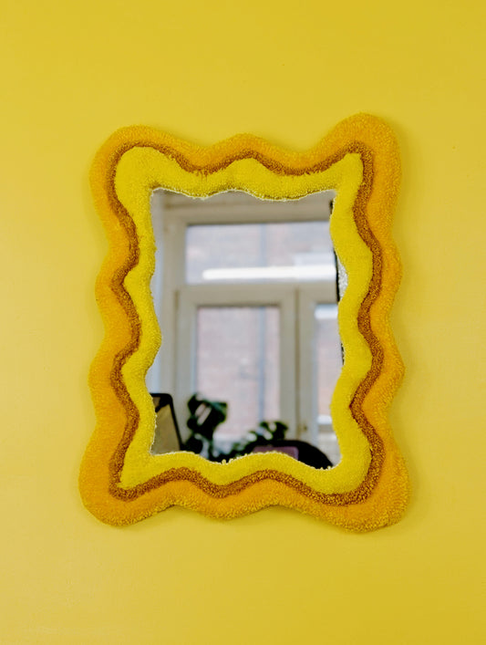 Handmade wavy tufted mirror with colourful textured frame in alternating shades of sunshine yellow, mustard yellow and bright yellow, modern aesthetic wall décor for home interiors.