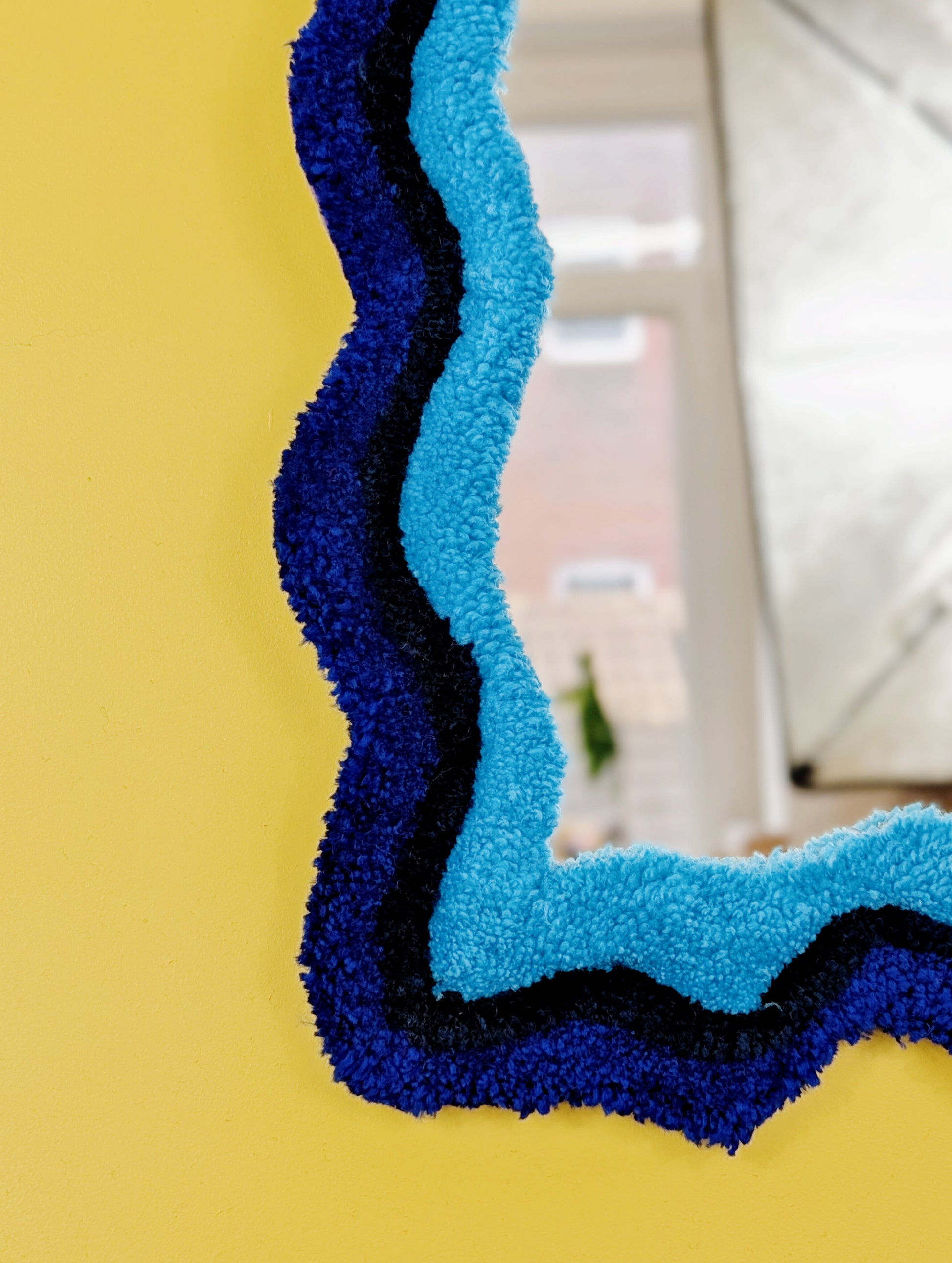 Handmade wavy tufted mirror with colourful textured frame in alternating shades of blue, modern aesthetic wall décor for home interiors.