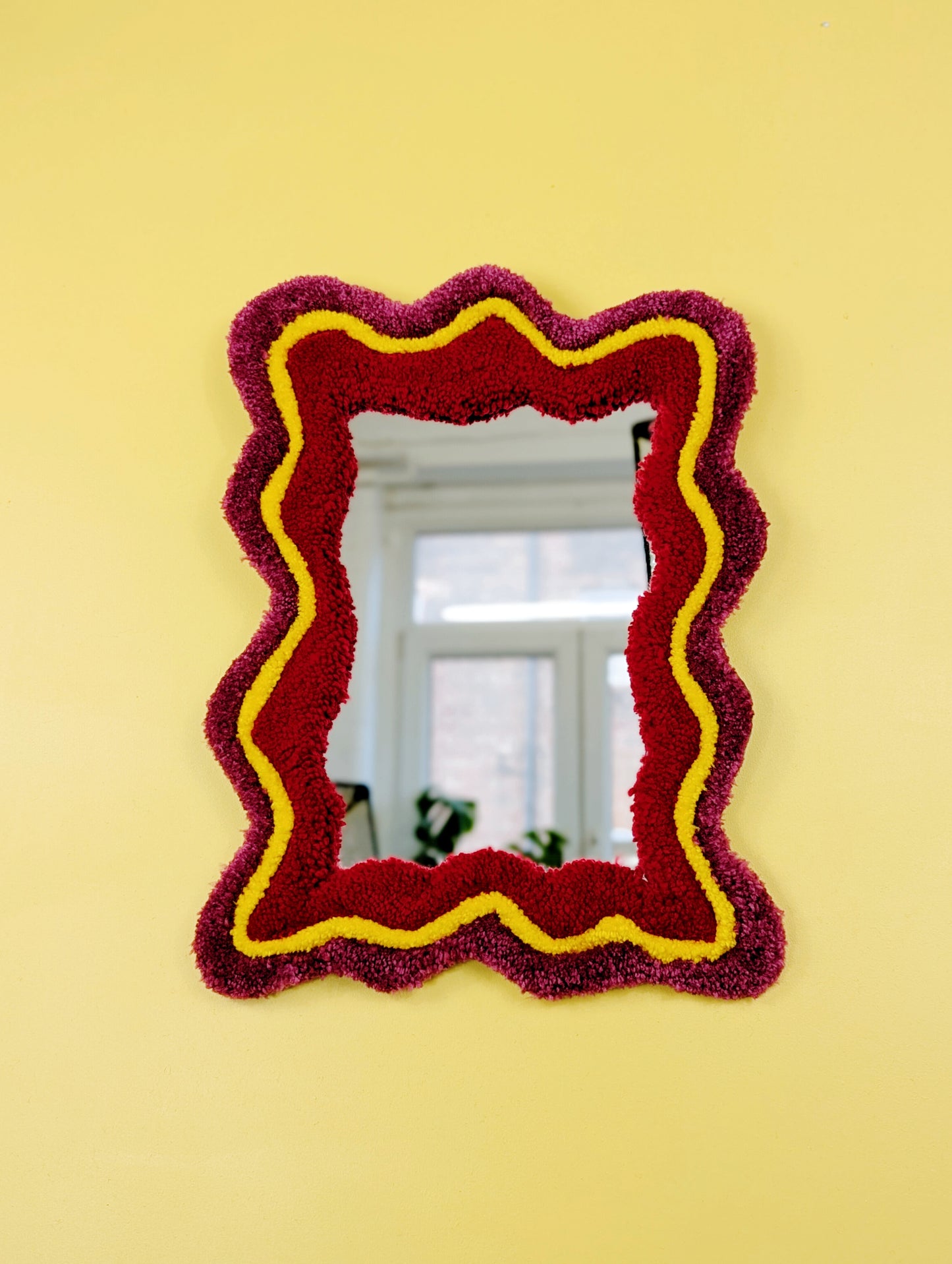 Handmade wavy tufted mirror with colourful textured frame in dark pink, bright yellow and red, modern aesthetic wall décor for home interiors
